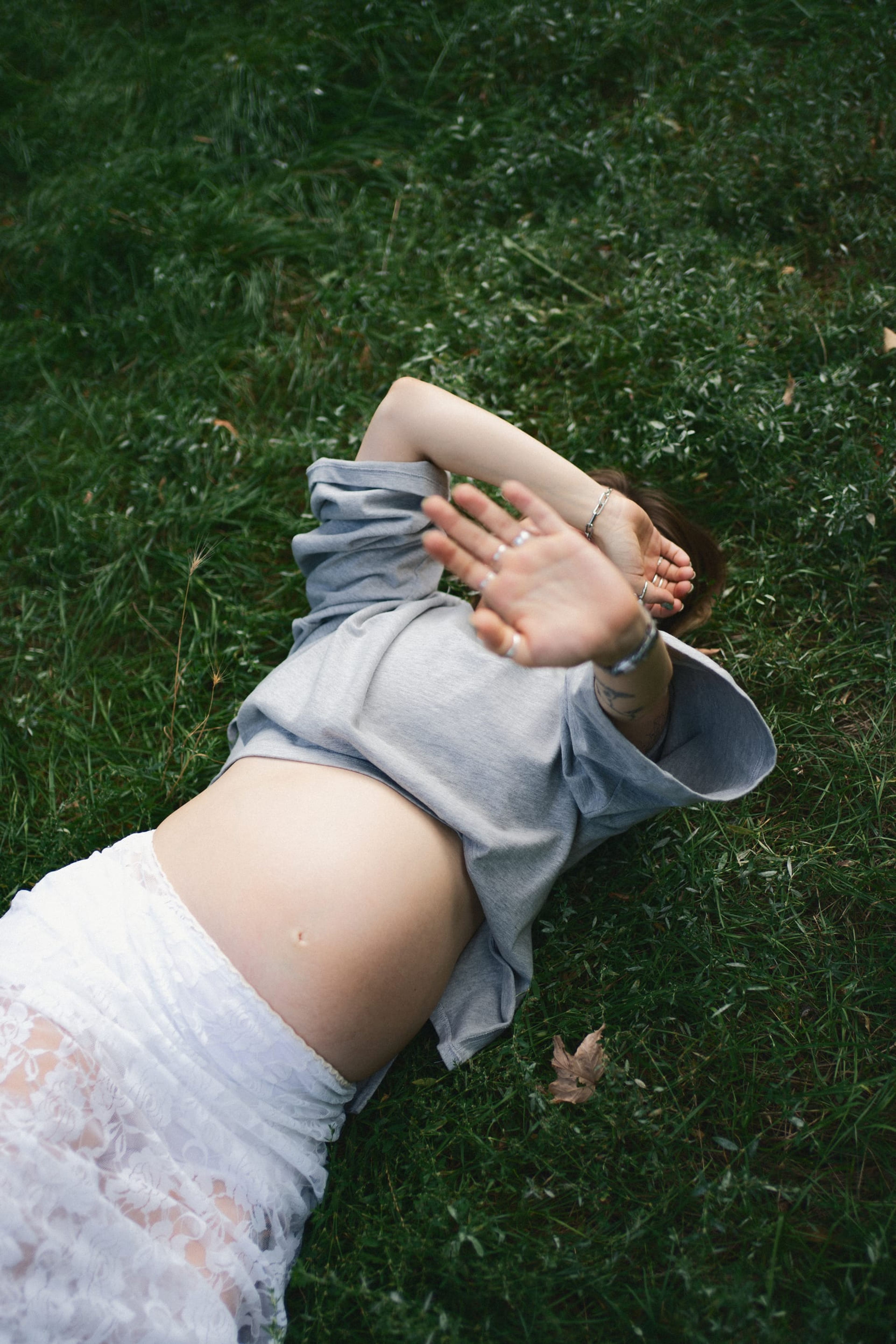 Expectant mother lying in the grass with one arm resting over her eyes