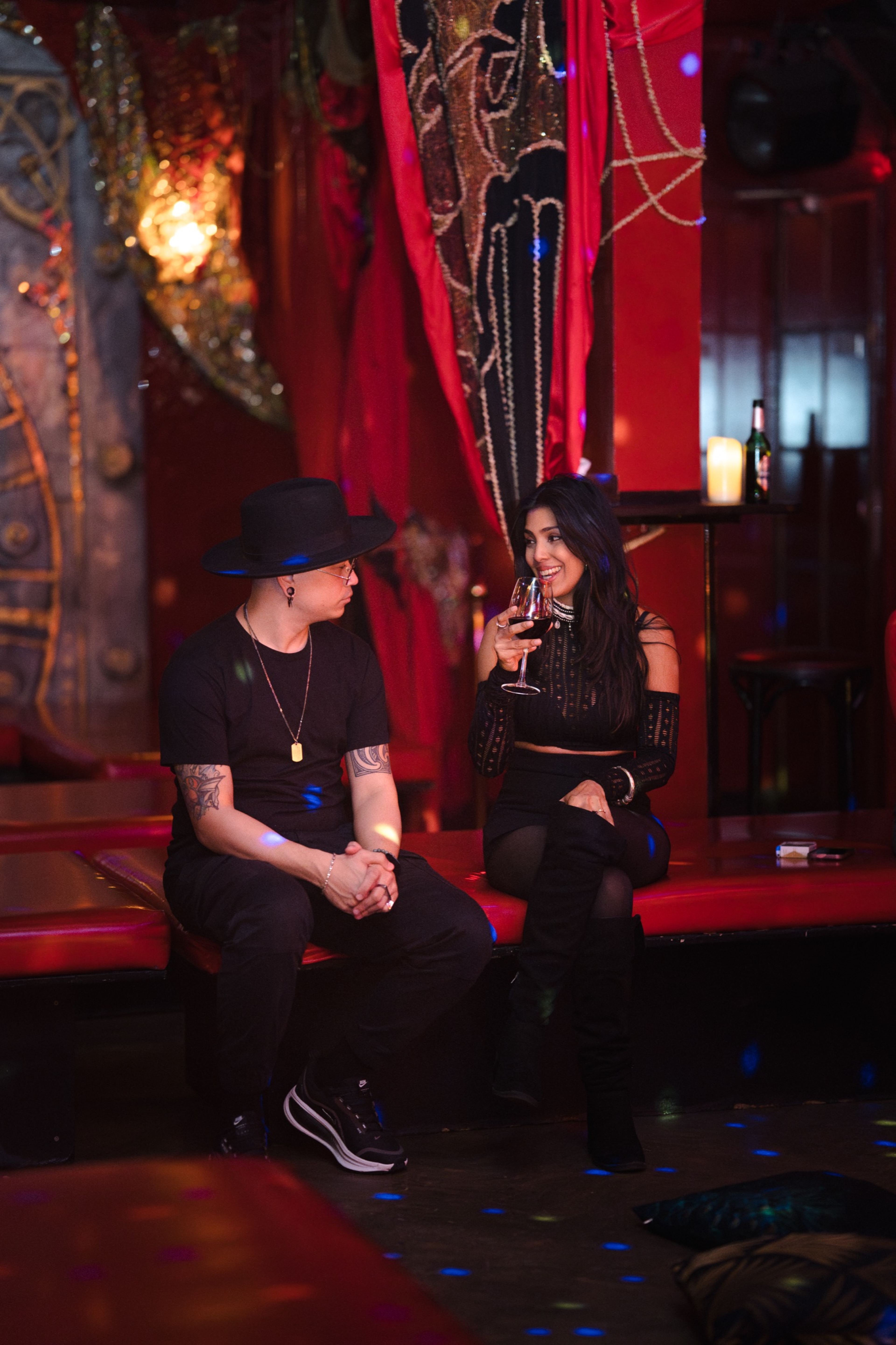 Two guests talking over wine on a red velvet sofa