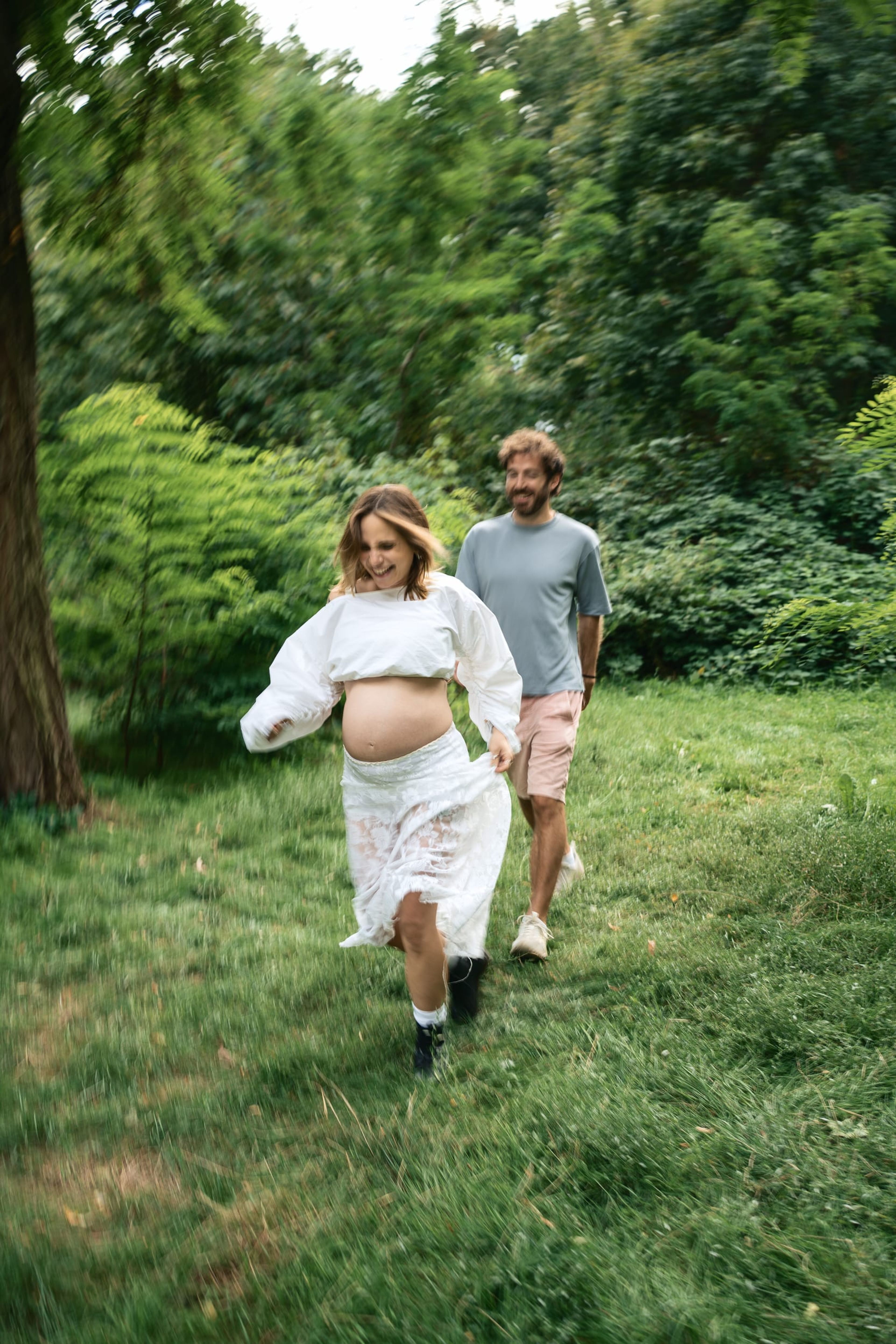Expectant couple walking through a sunlit meadow toward the camera