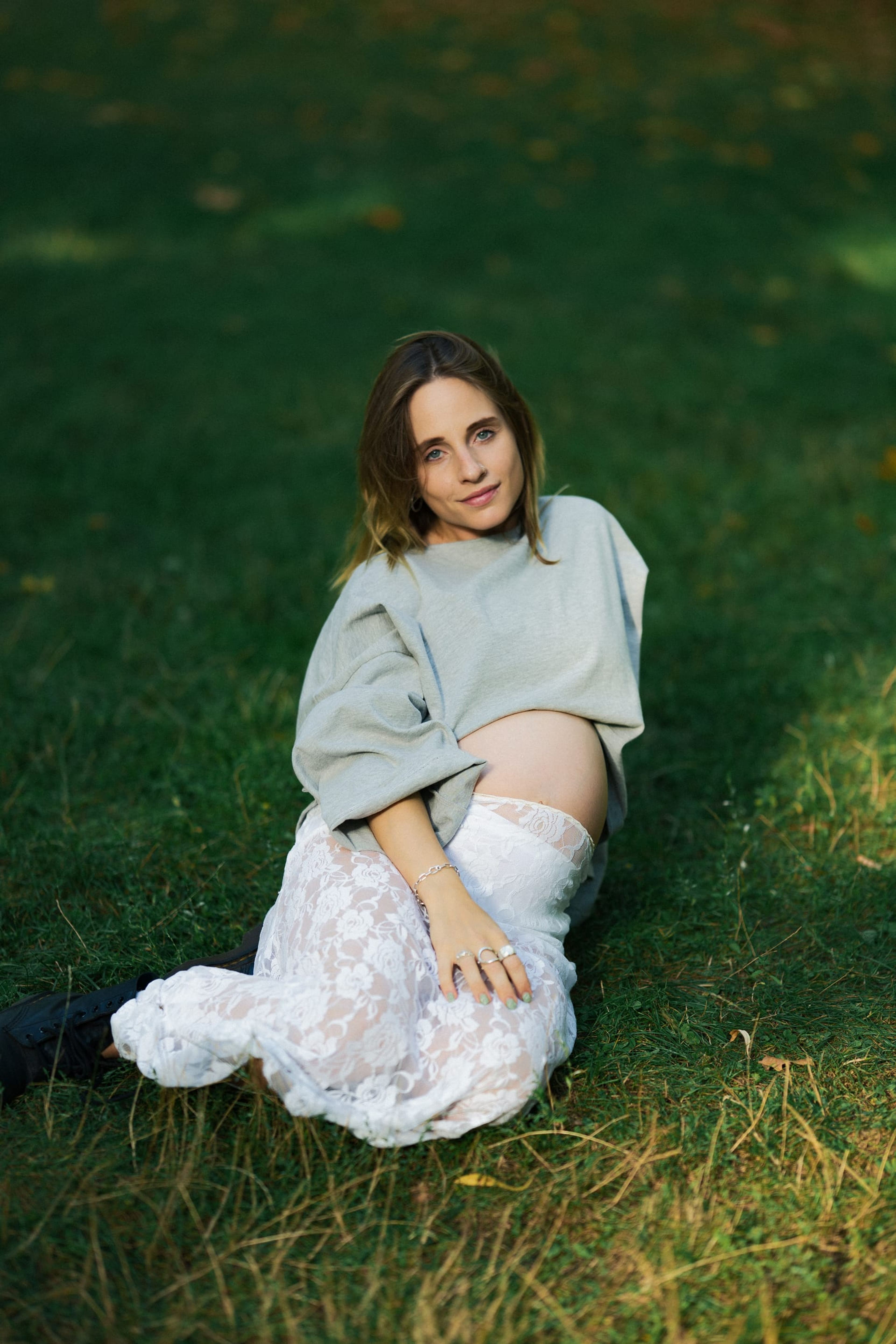 Expectant mother sitting in the grass at golden hour, looking to camera