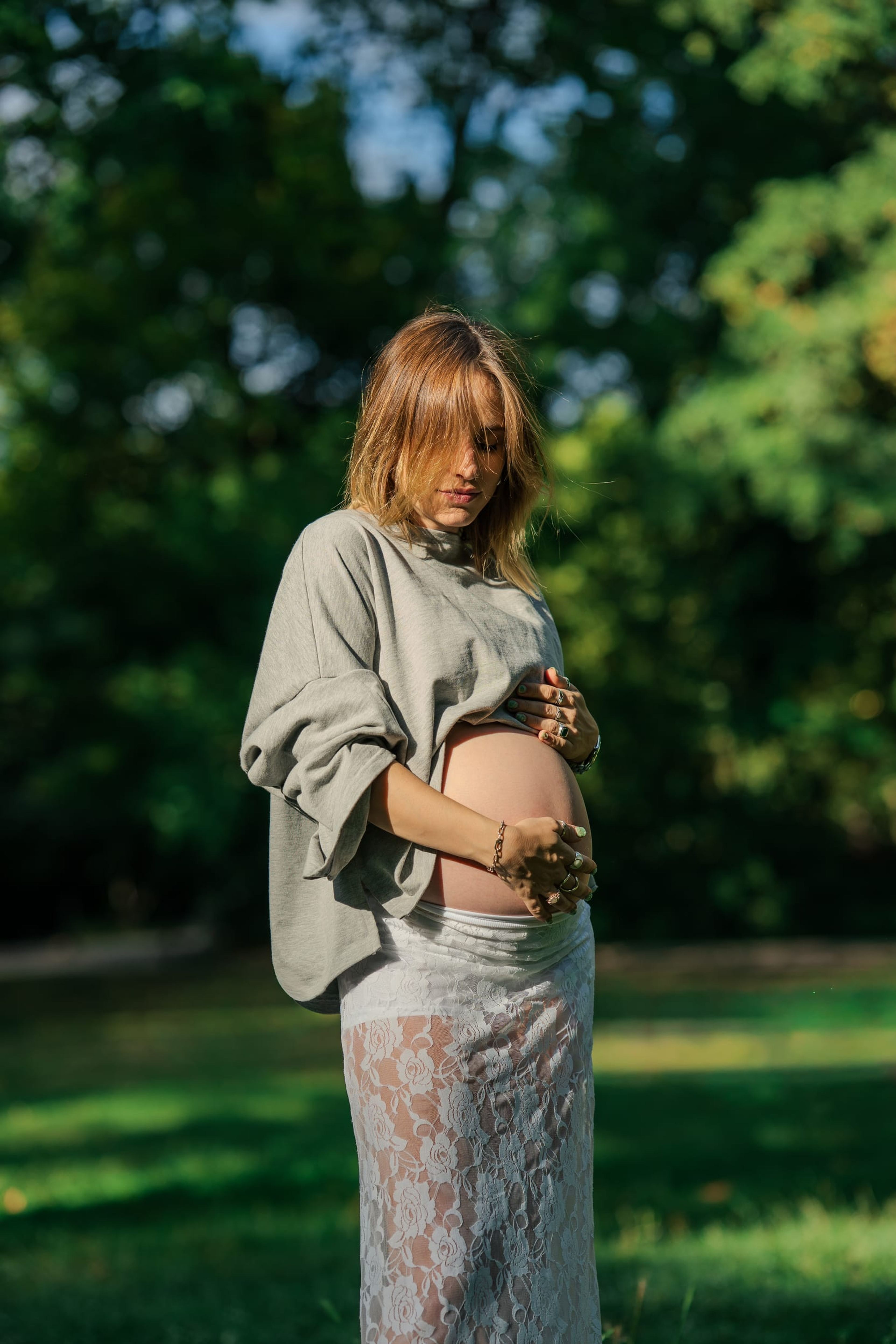 Expectant mother standing among the trees, holding her belly and looking down