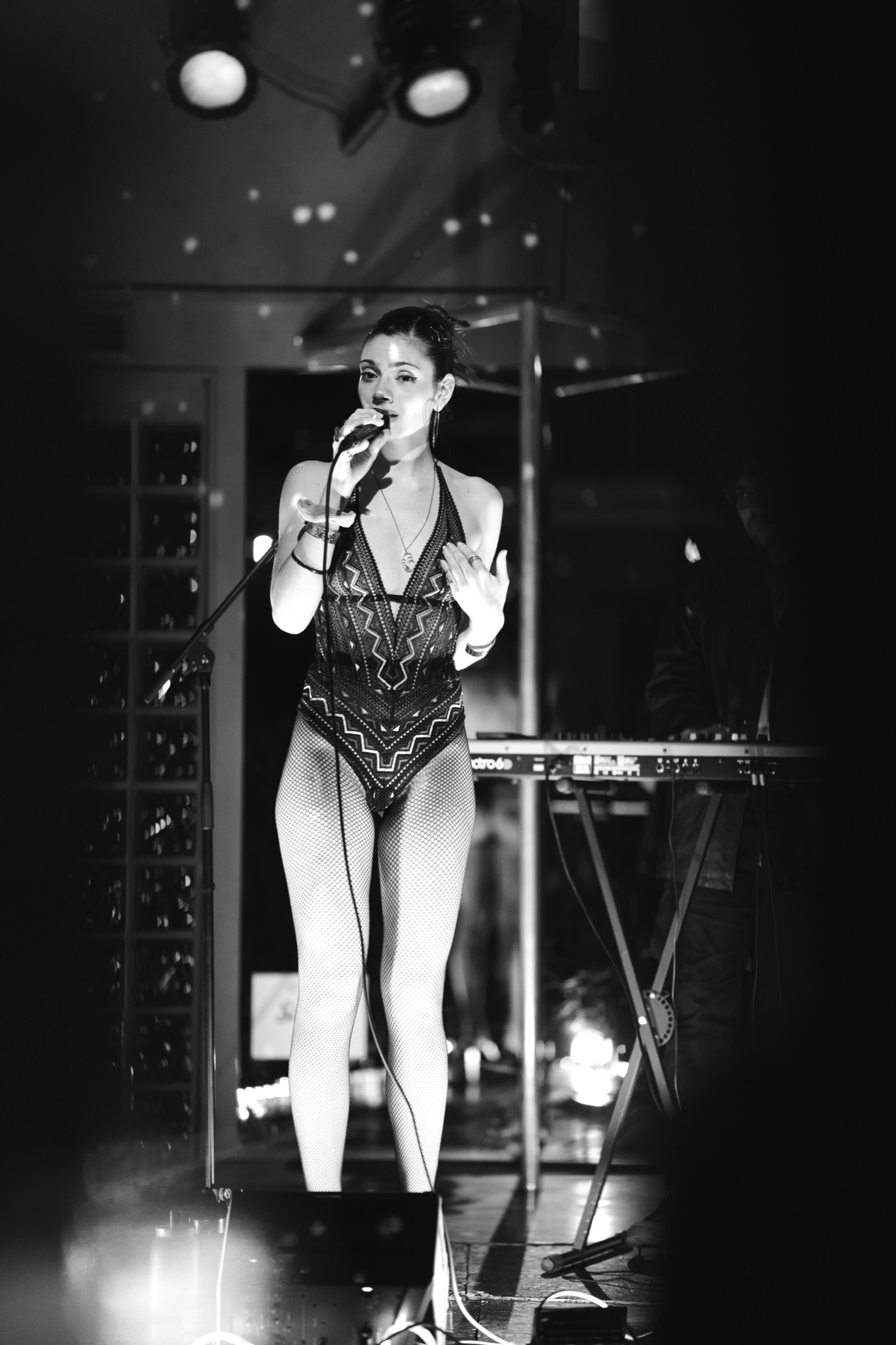 Vocalist singing beside a keyboard, in black and white