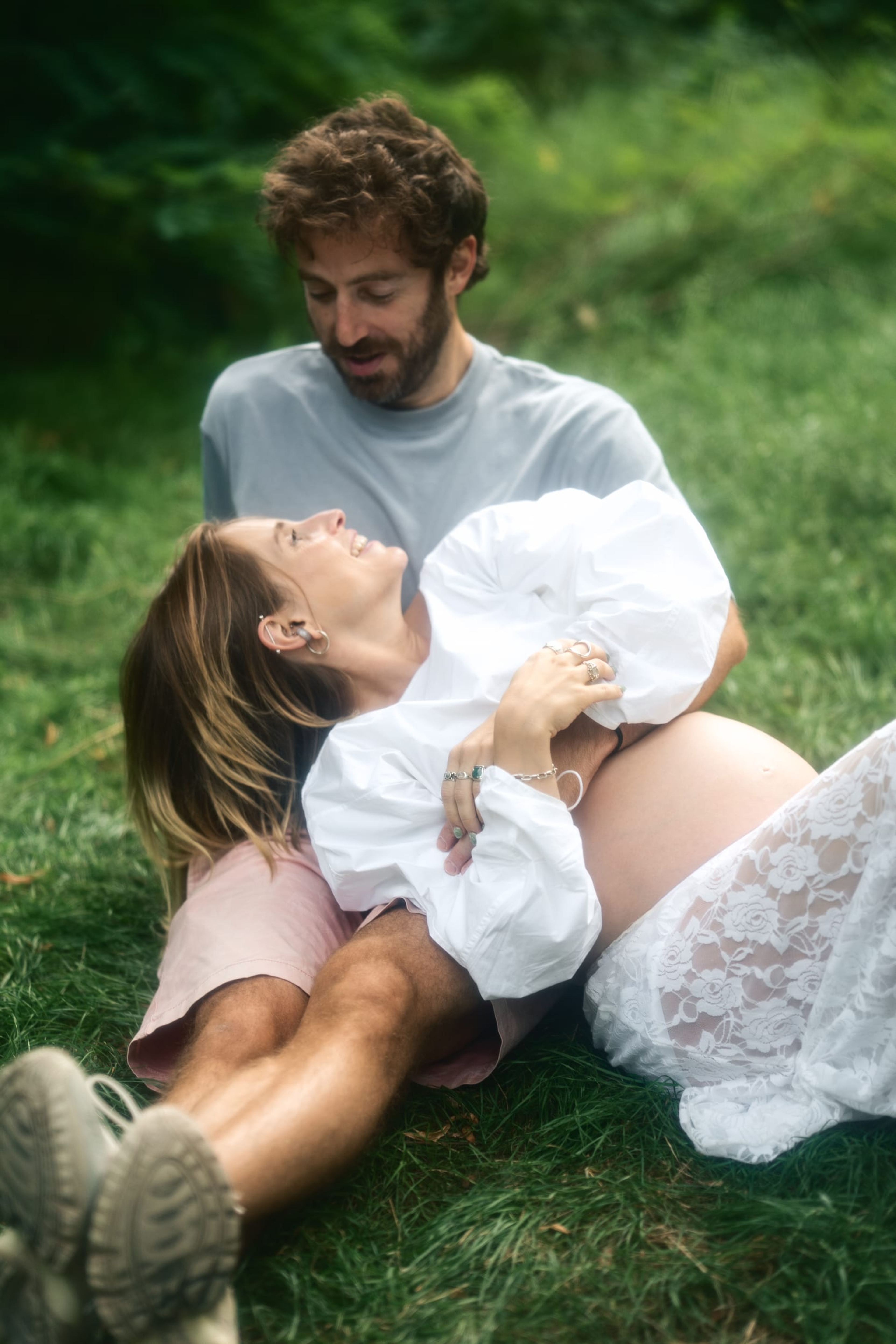 Expectant couple lying in the grass as she looks up at him