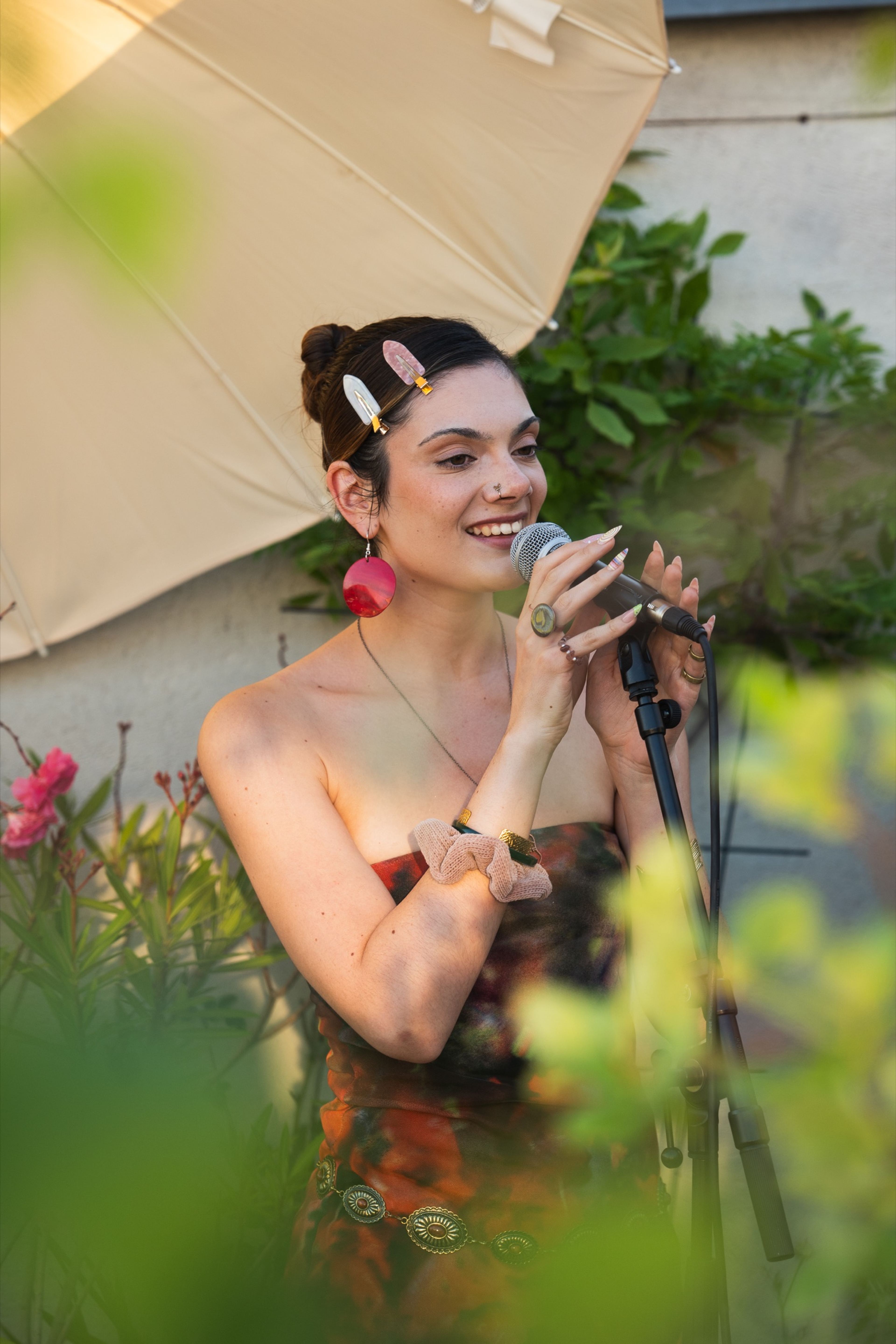 Smiling singer at the microphone beneath a parasol at a Her Sound rooftop session