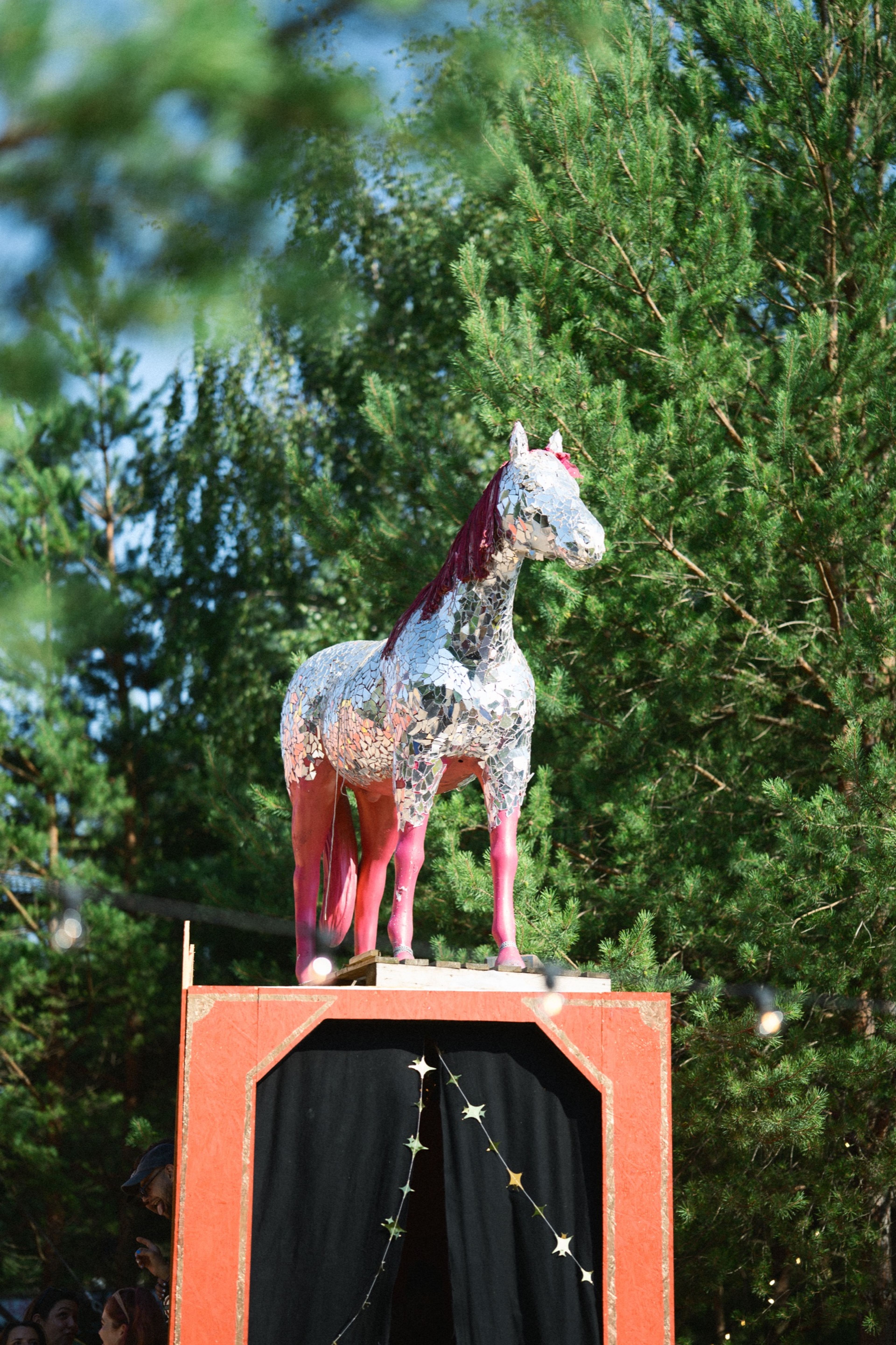 A mirror-mosaic horse sculpture with pink legs on a red plinth