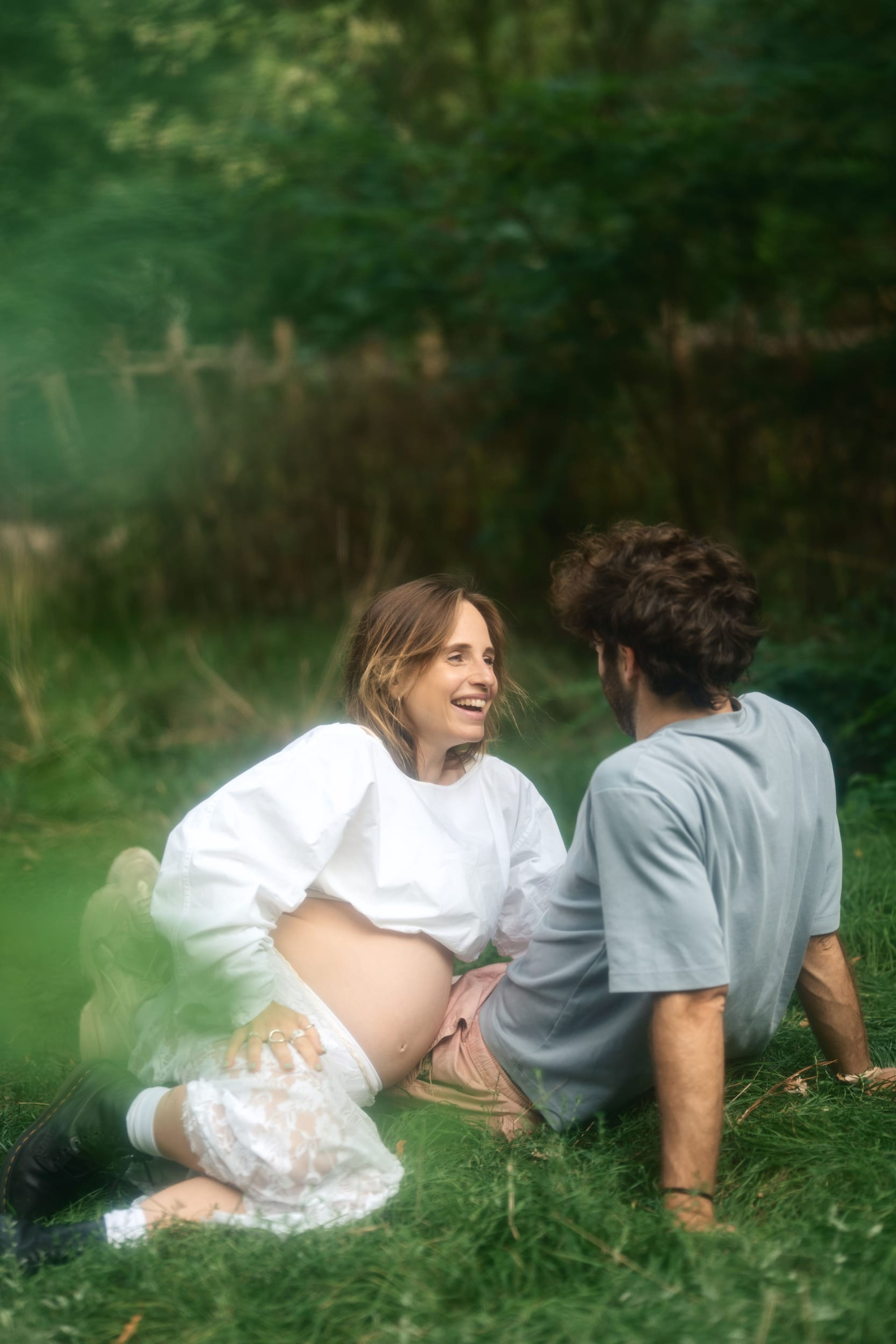 Expectant couple sitting facing each other in a misty green clearing