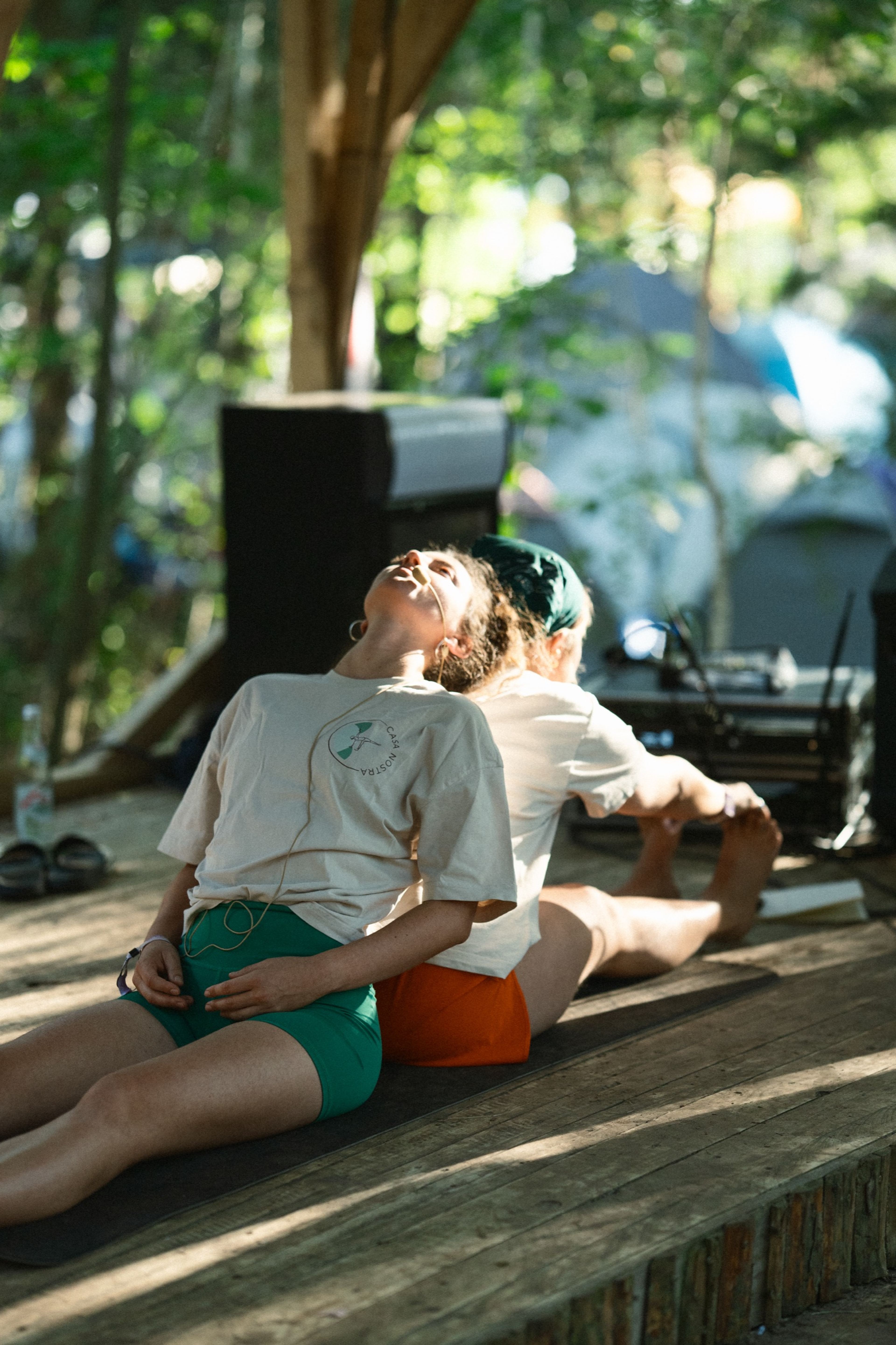 Two people stretching back-to-back on a wooden deck in golden light