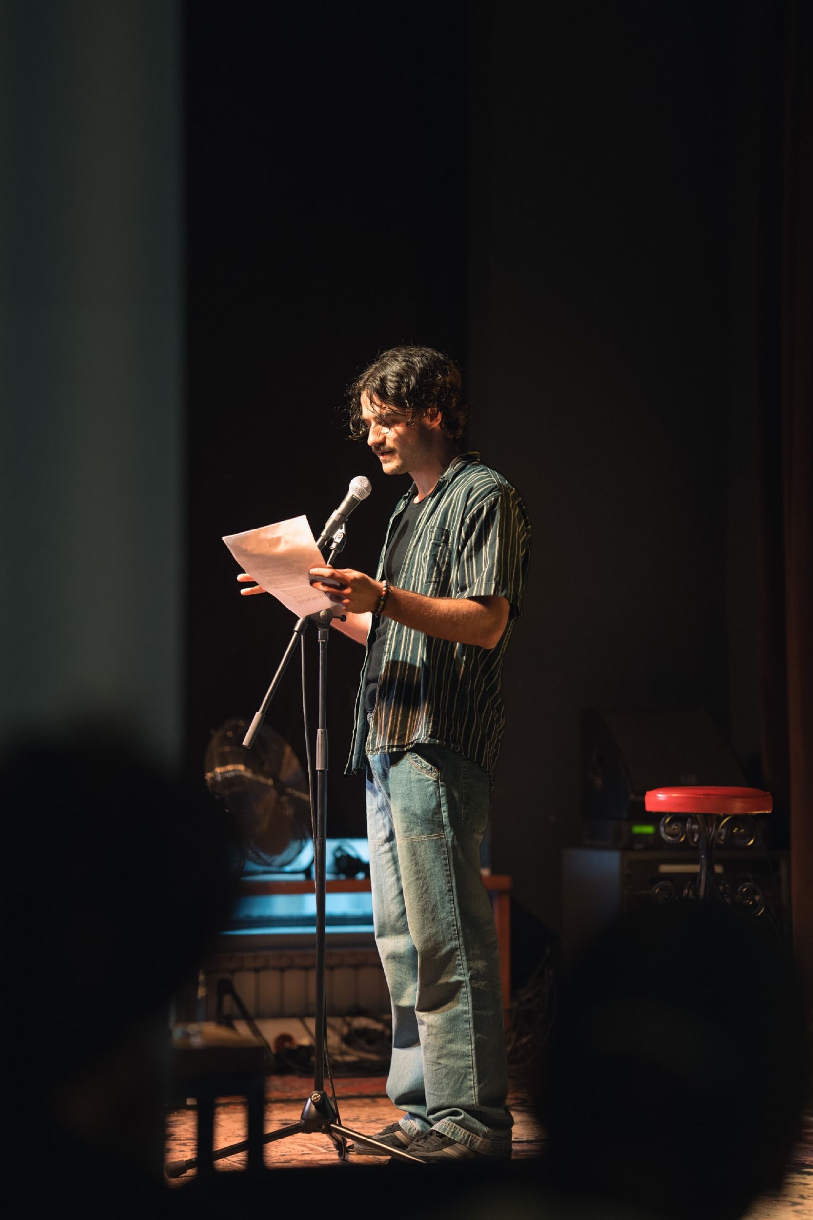 Speaker reading a story from a page under the stage lights at Seanchoíche in Berlin