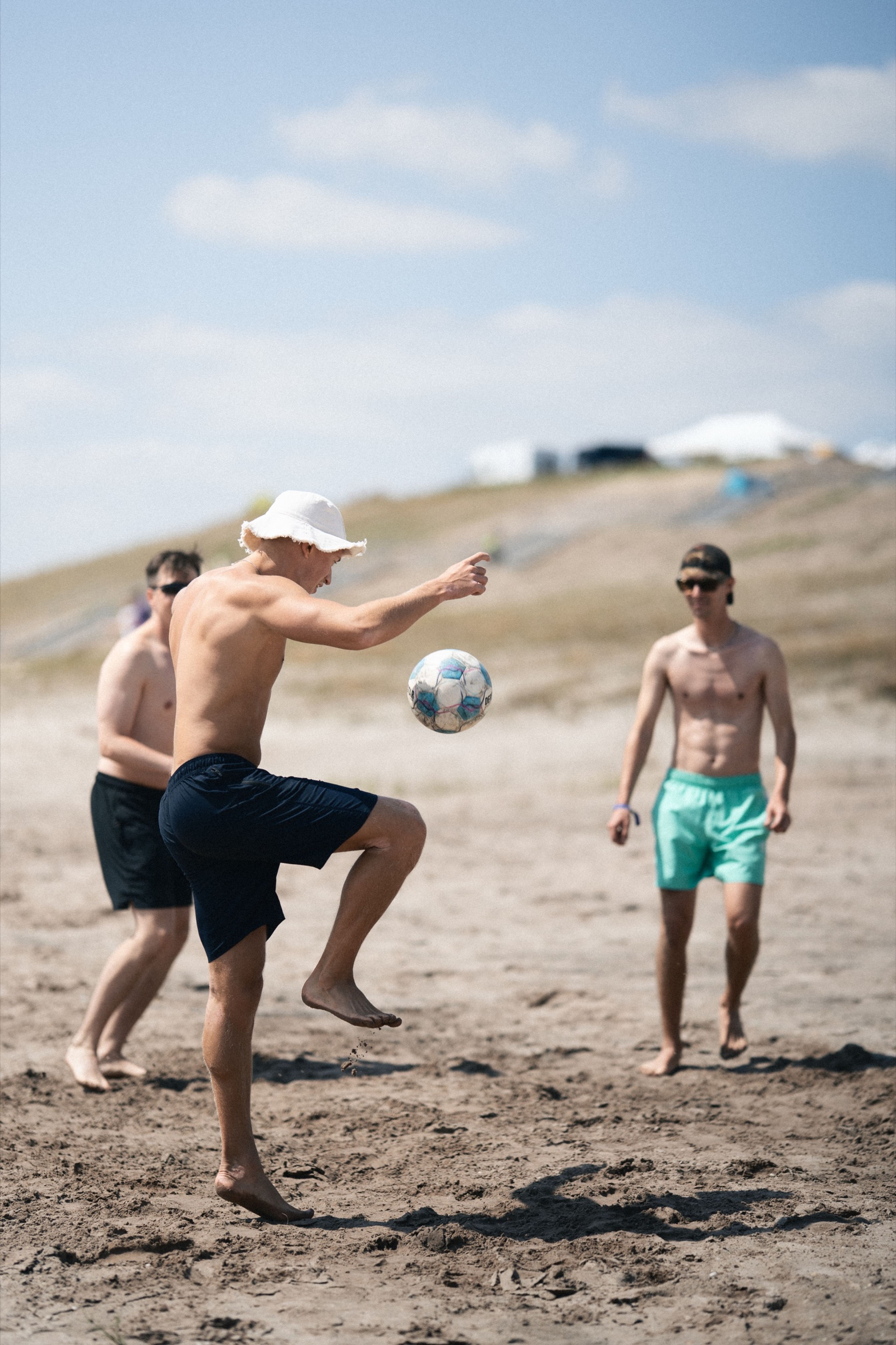 Friends playing football barefoot on the lake beach