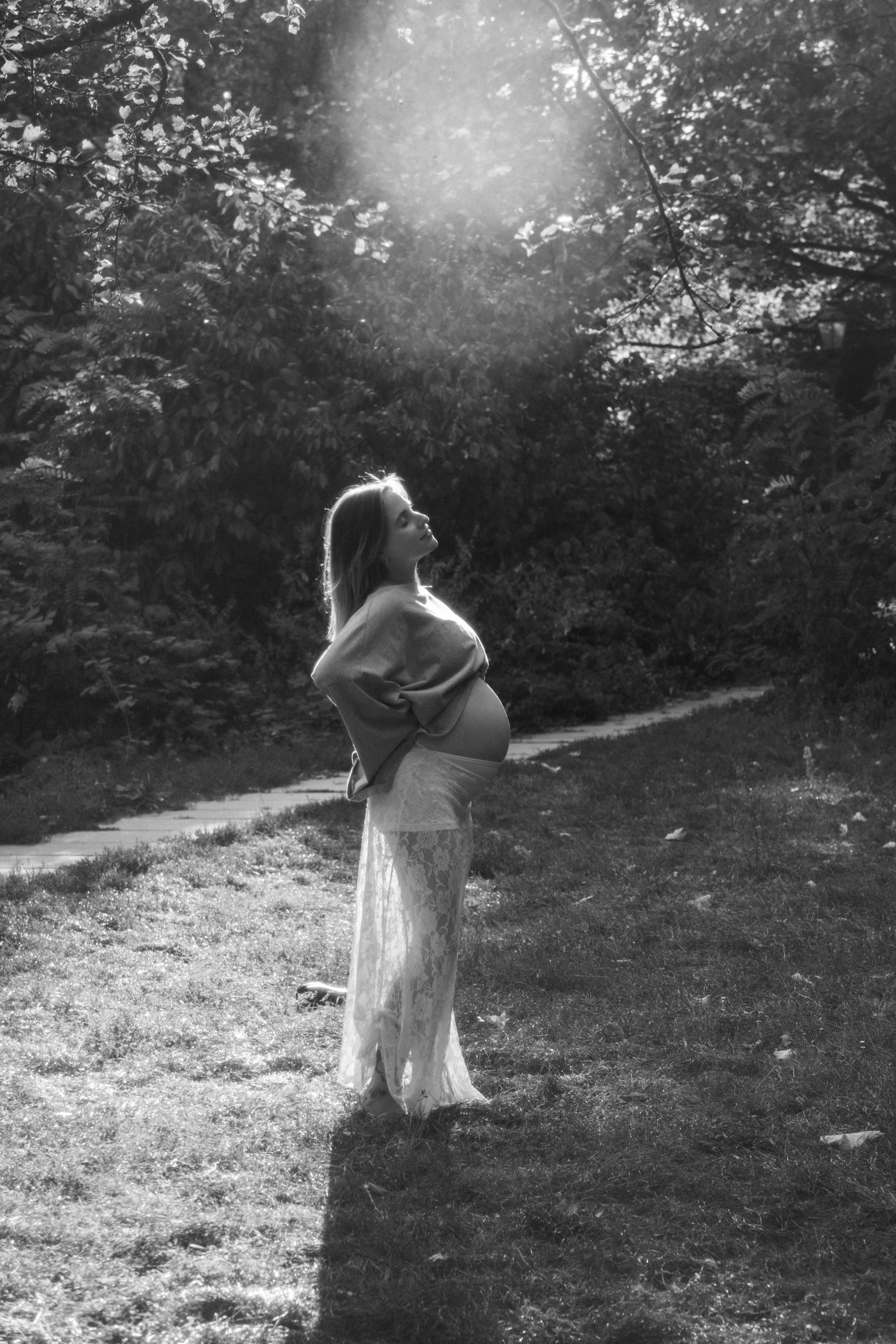 Black-and-white portrait of the expectant mother standing in a sunburst, looking up