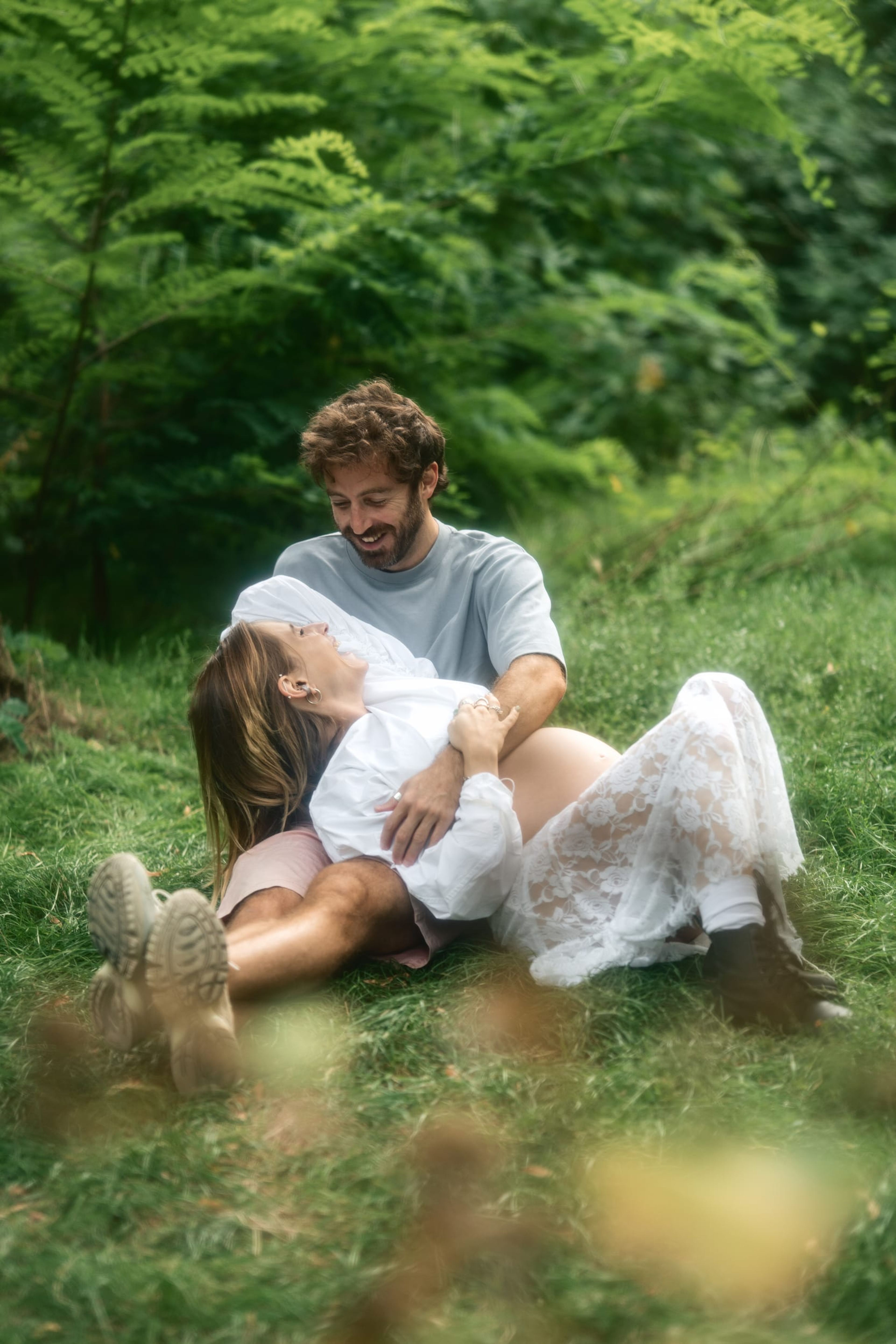 Expectant couple lying together in the grass, laughing