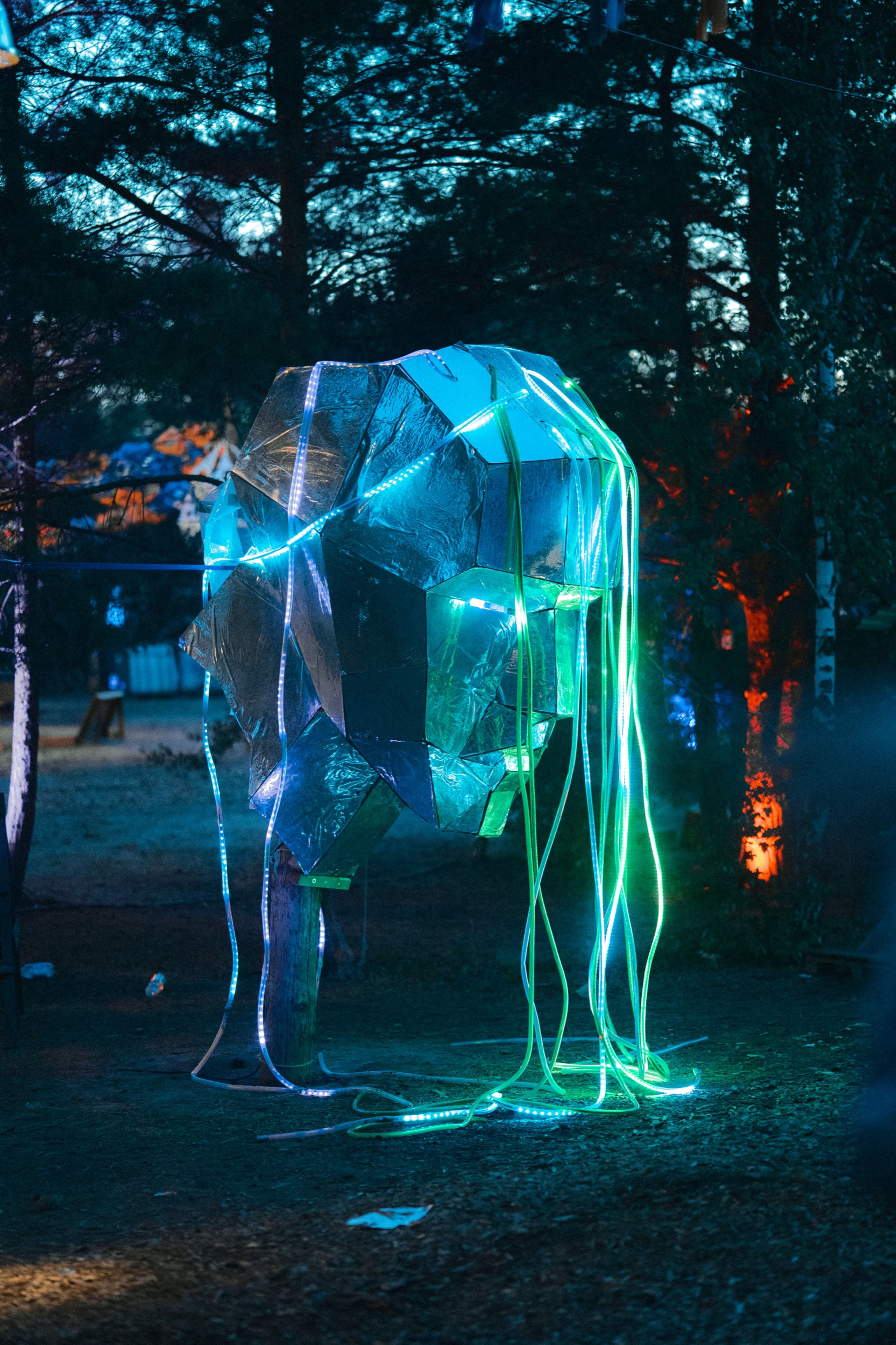 An illuminated sculpture strung with green and blue light at night