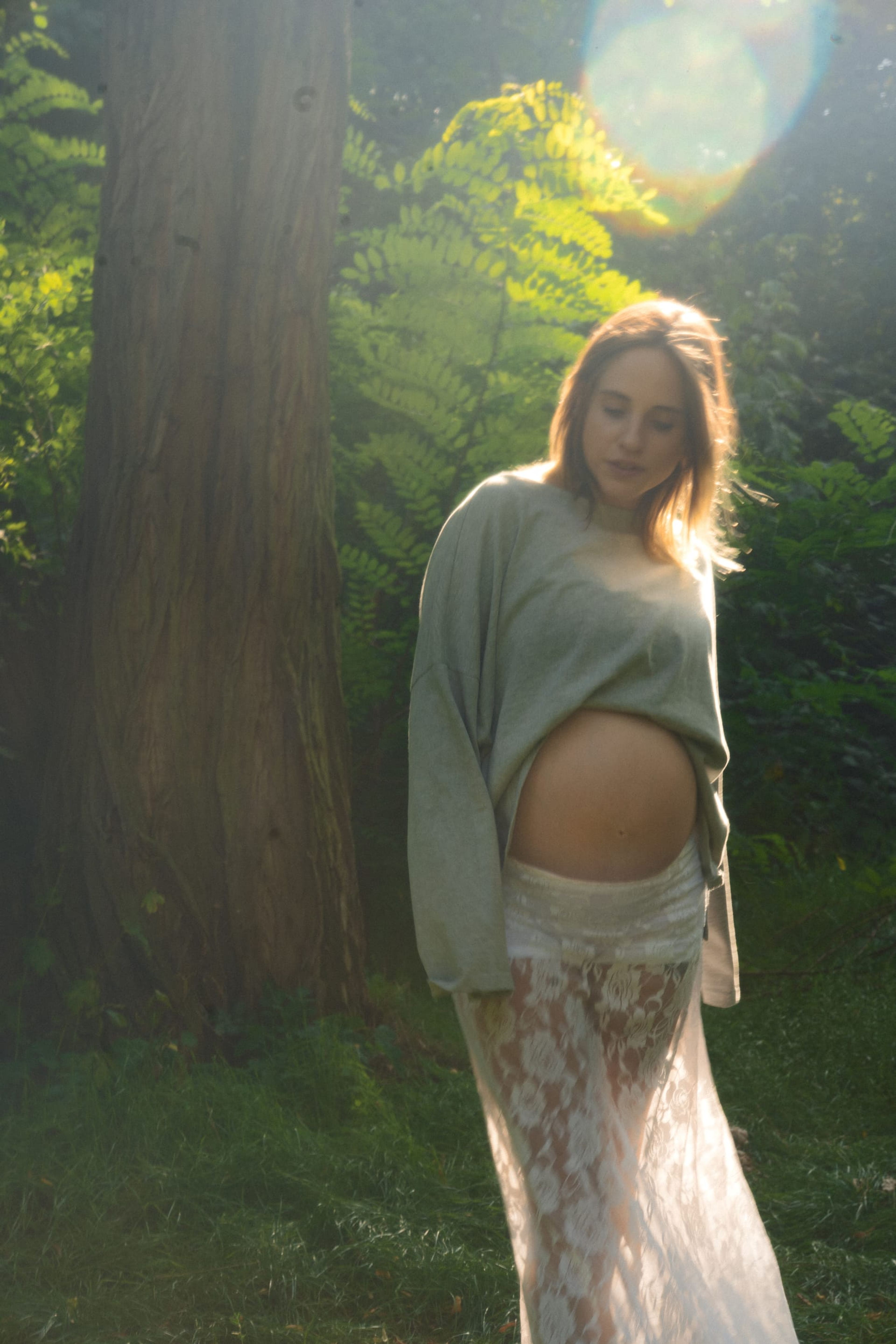 Expectant mother in soft backlight, her sweater lifted to show the bump