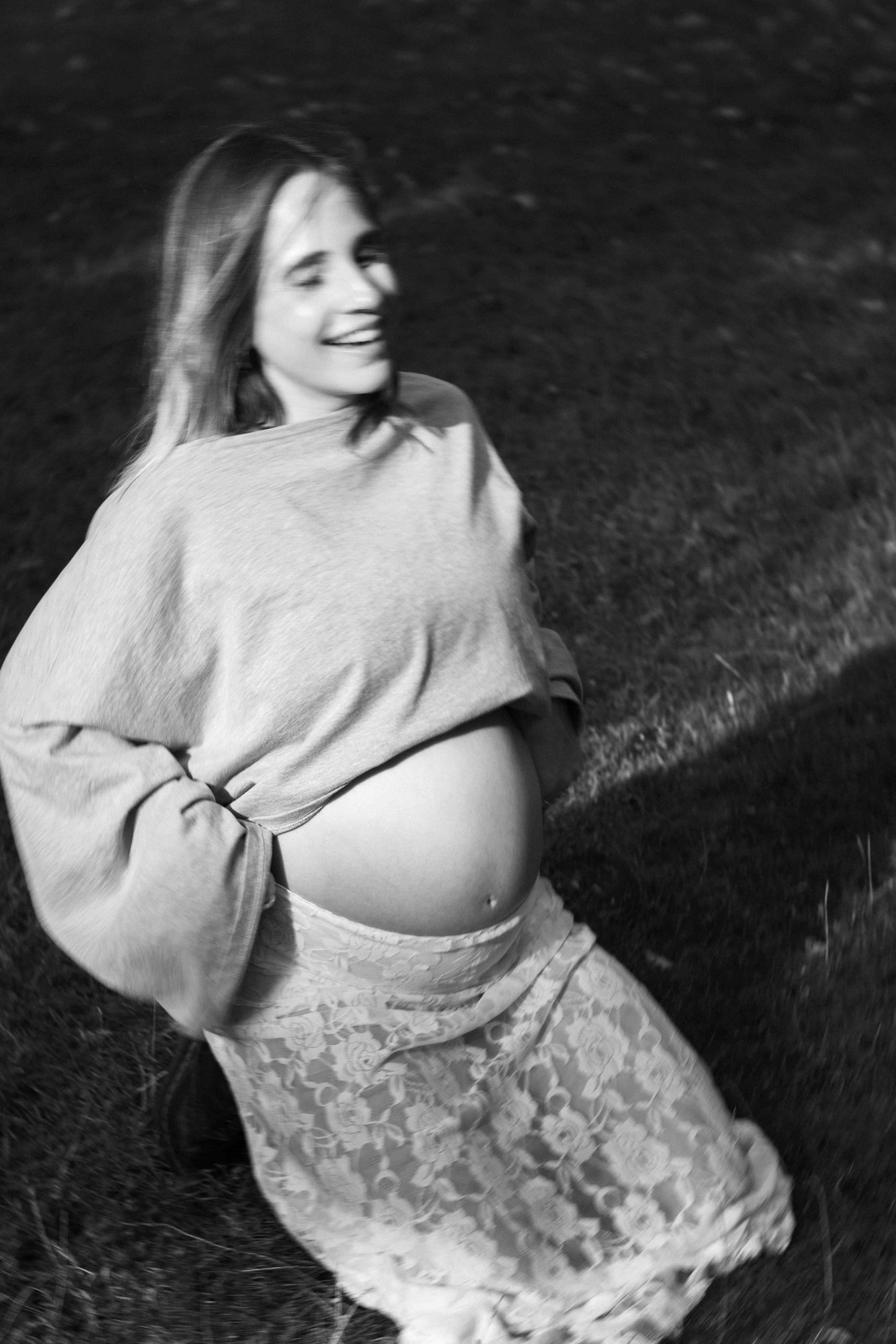 Black-and-white portrait of the expectant mother kneeling in the grass, laughing