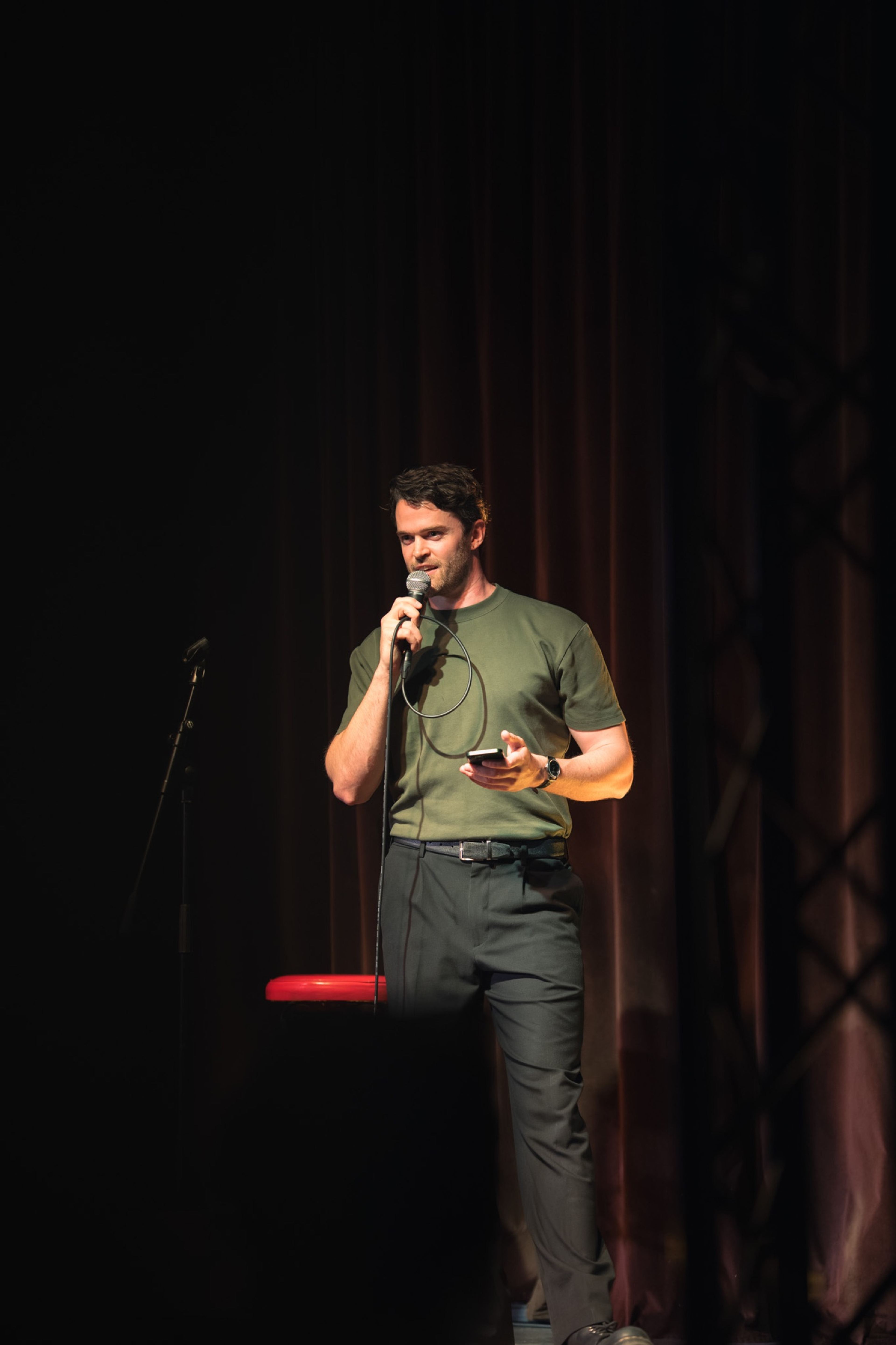 Storyteller in an olive shirt on the dark stage, microphone in hand
