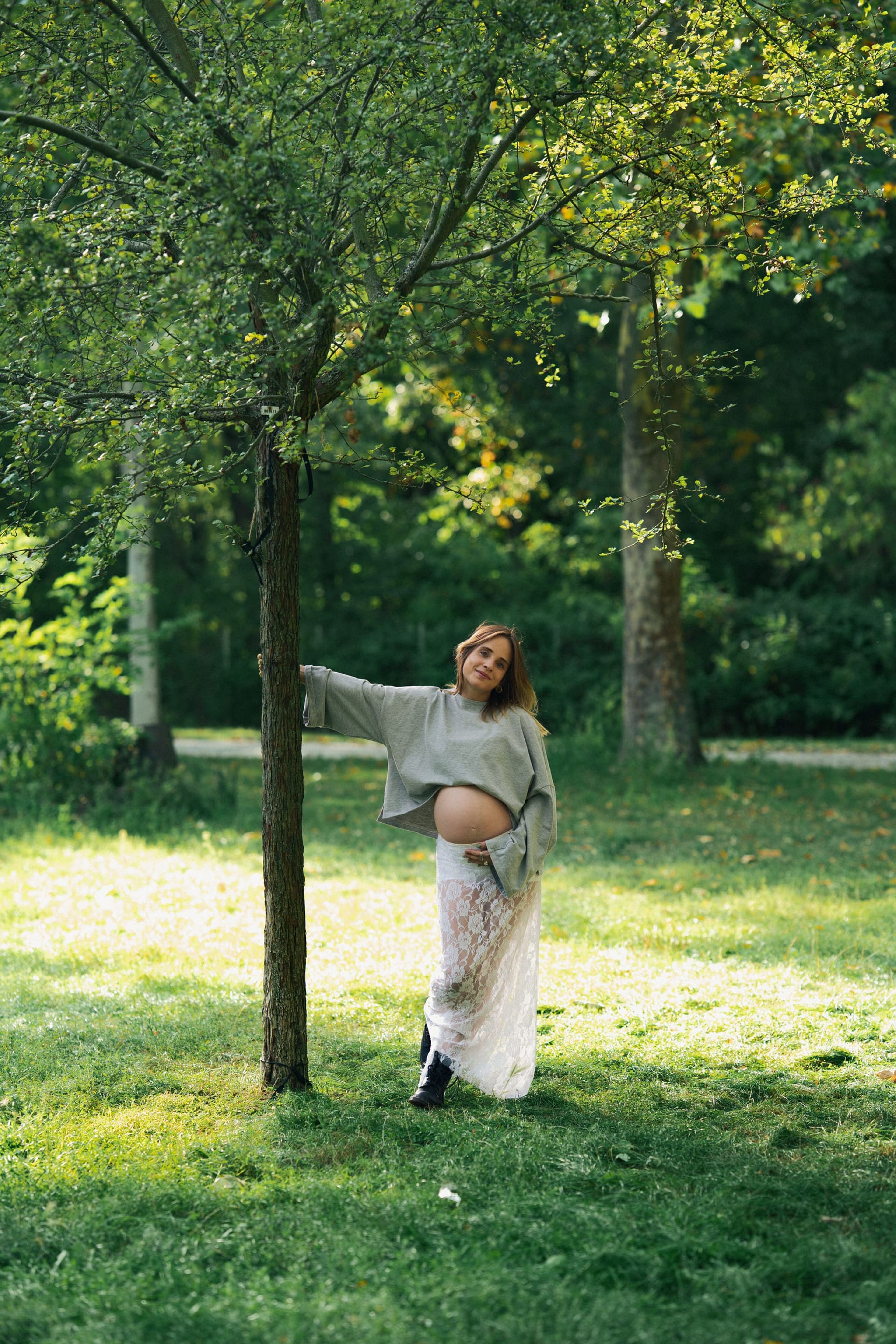 Expectant mother standing beside a young tree in a green park
