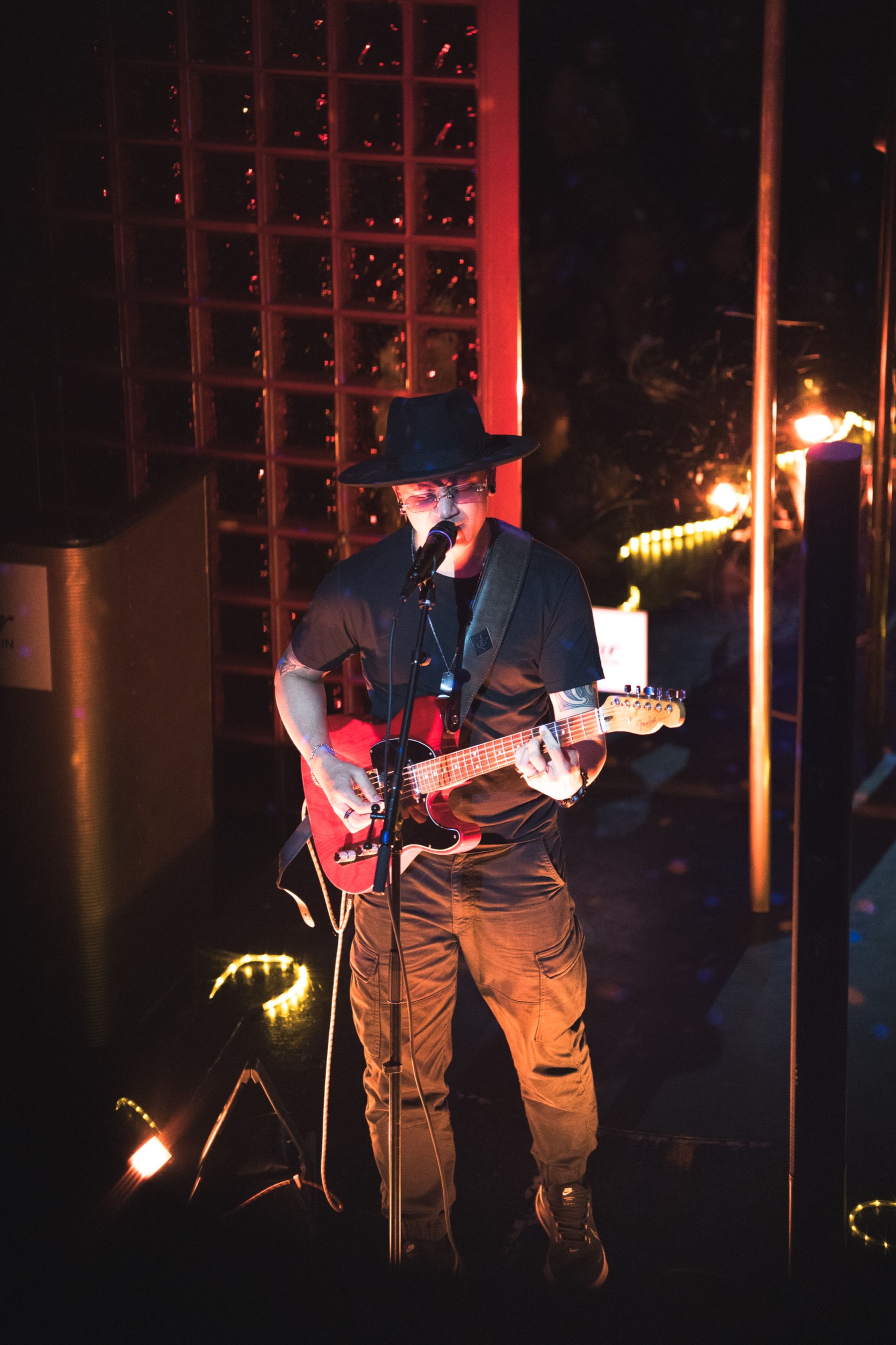 Guitarist in a wide-brimmed hat performing with a red electric guitar