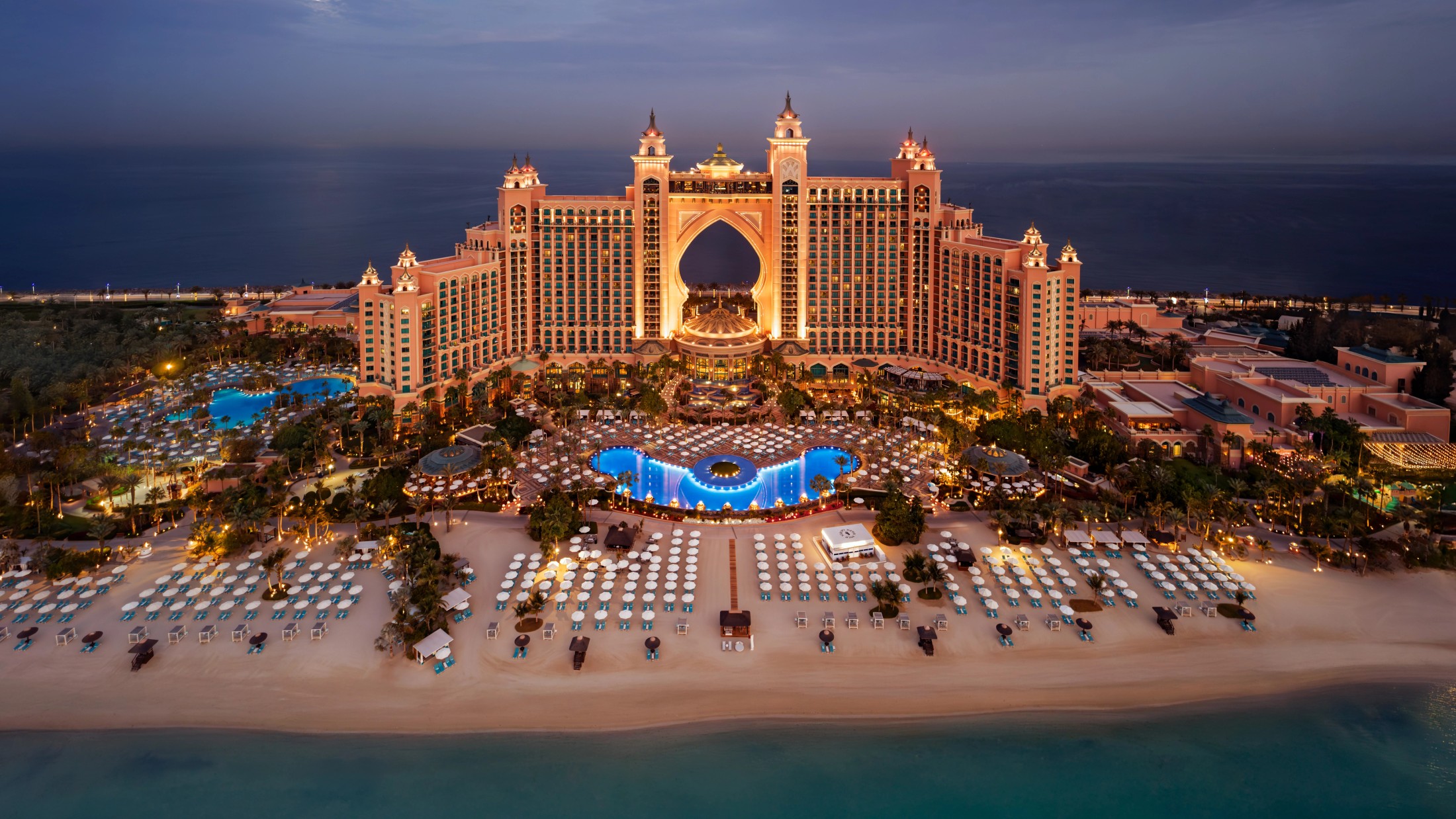 Atlantis The Palm lit up at dusk above its beach
