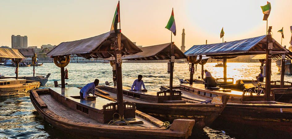 Wooden abras moored along Dubai Creek at sunset, flags flying from their canopies