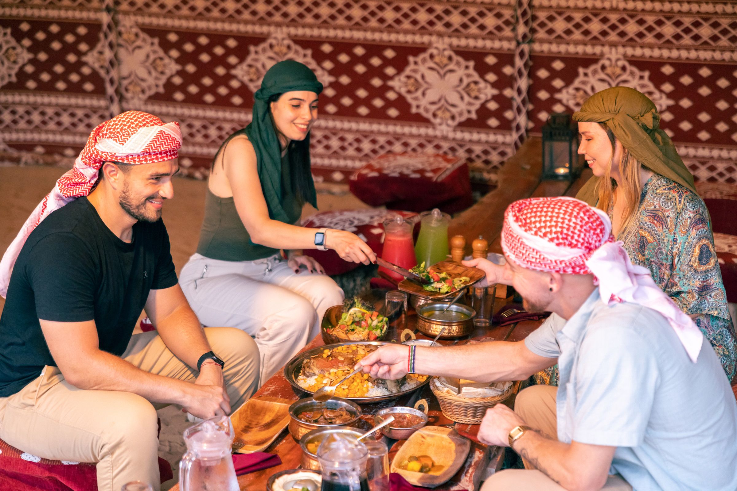 Guests in keffiyehs sharing a traditional dinner with their host in a desert camp majlis