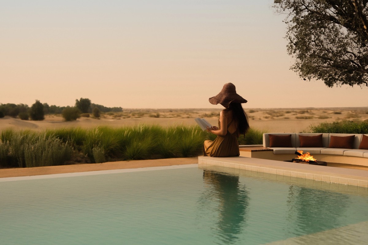 A guest reading beside a desert pool villa at Bab Al Shams at sunset