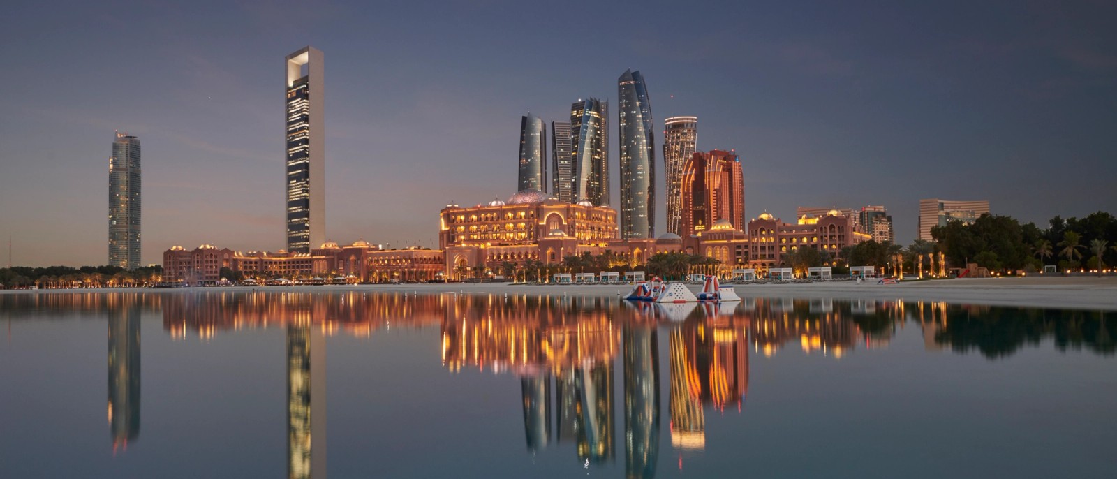 Abu Dhabi's skyline at dusk, reflected in the still water of the Gulf