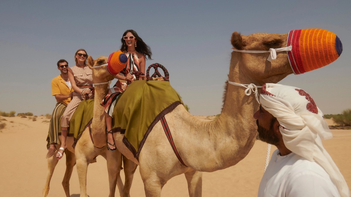 Travelers on a camel ride across the sand, led by a guide