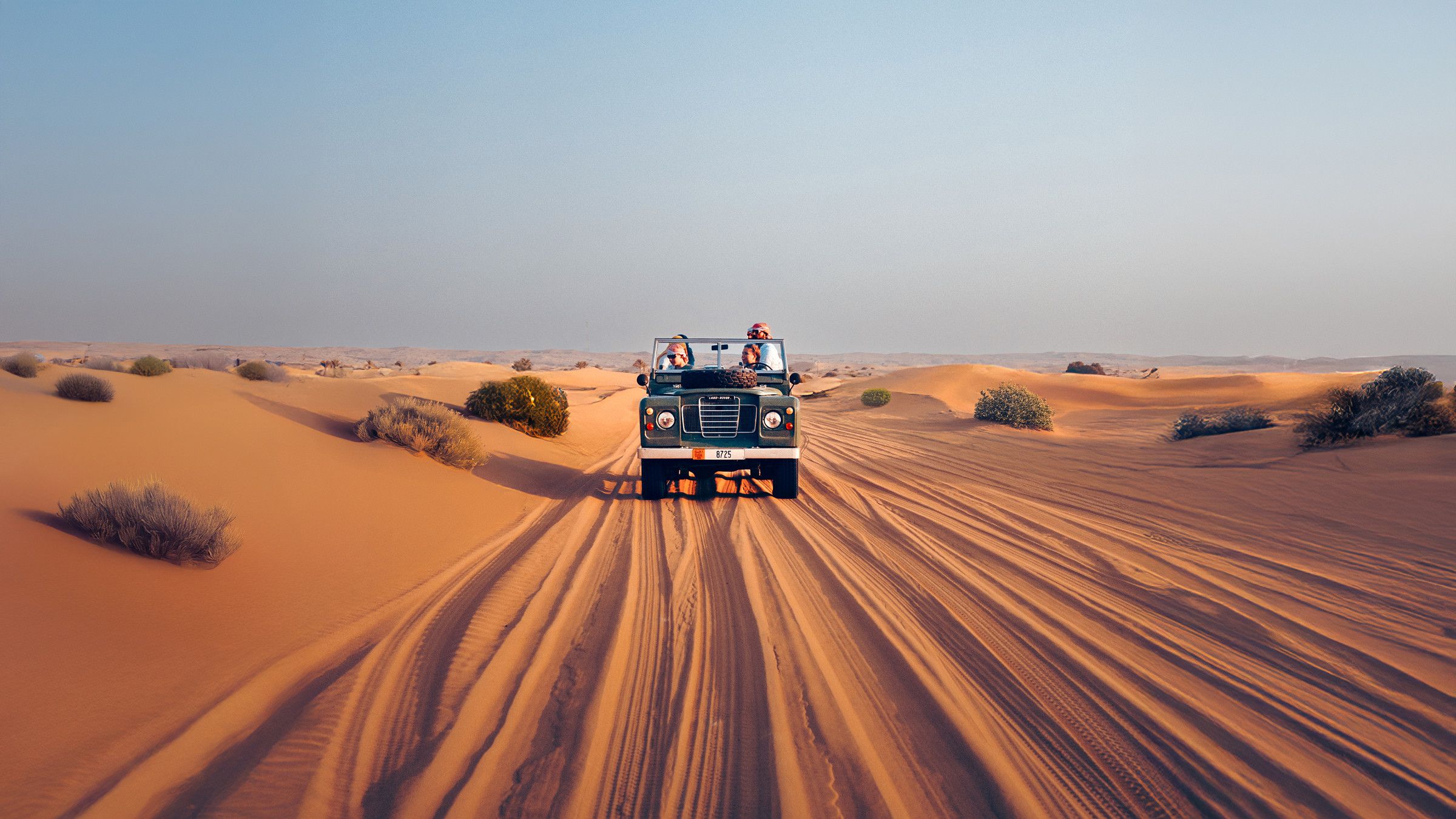 A vintage Land Rover crossing the dunes at sunset