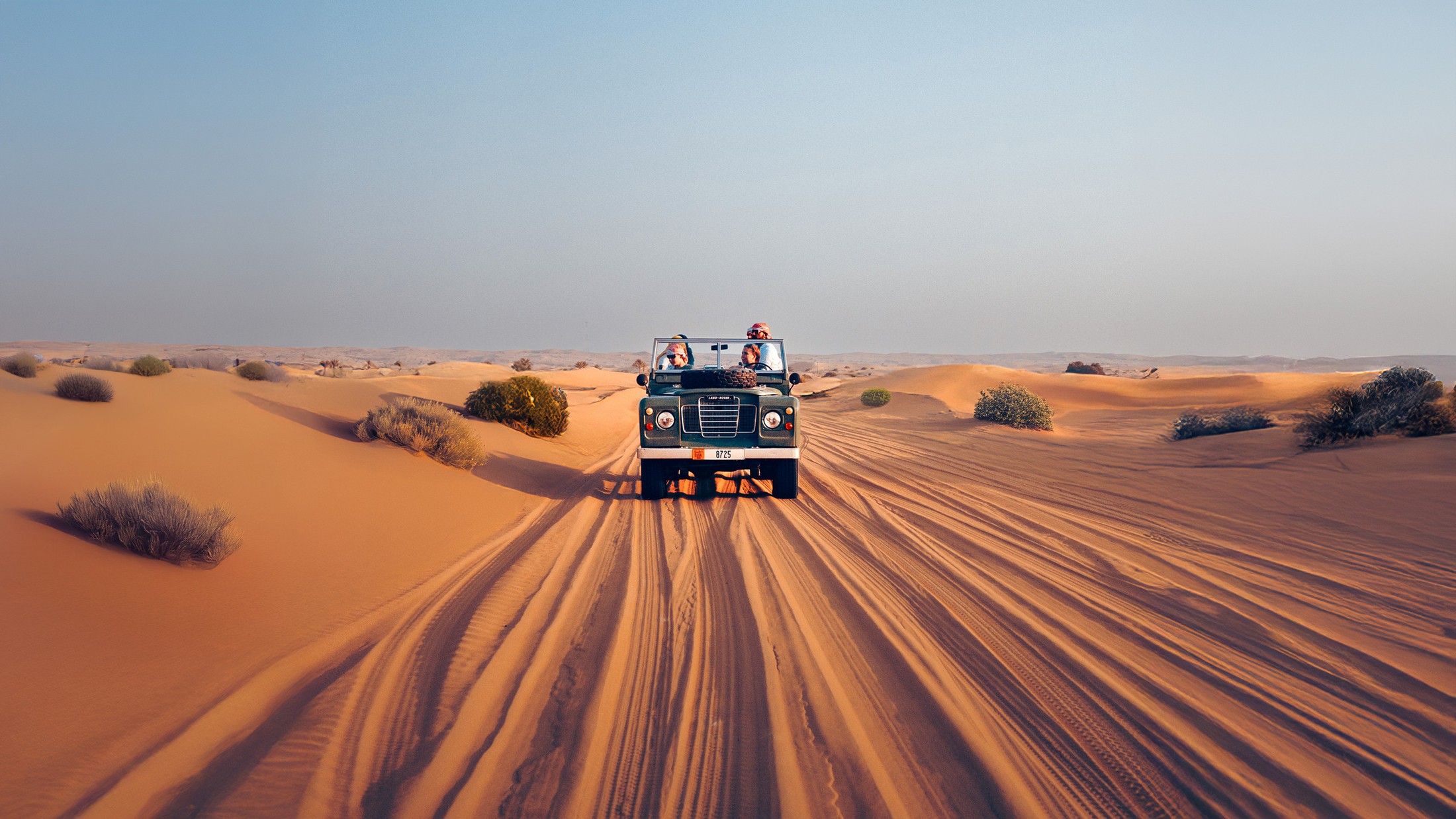 A vintage Land Rover crossing the dunes at sunset