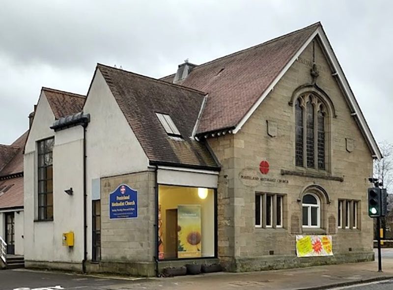 A stone Methodist church with a large traceried window and a modern rendered extension, on a street corner