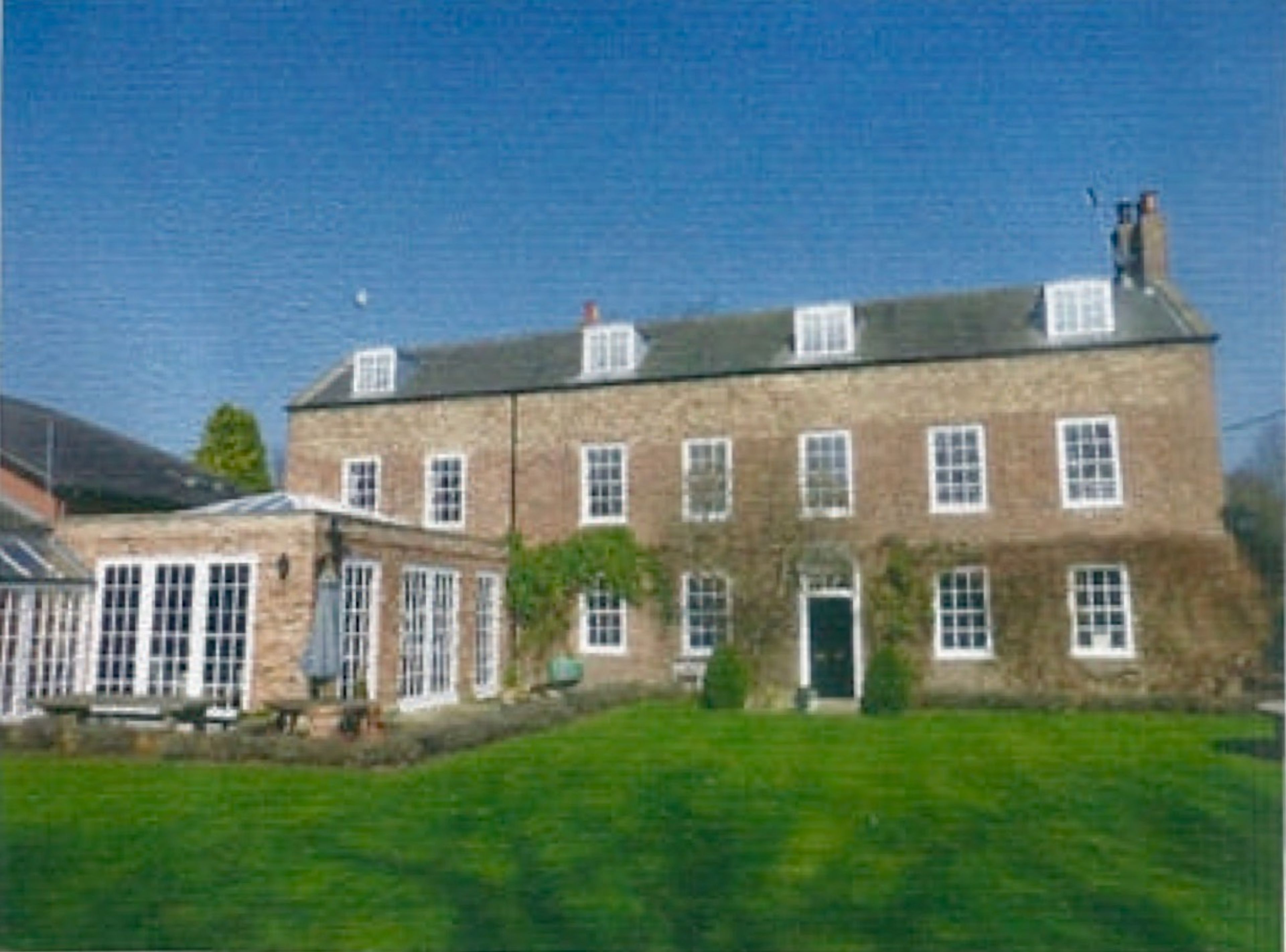 A large stone Georgian house with dormer windows and a central door, a glazed conservatory to one side and lawn in front