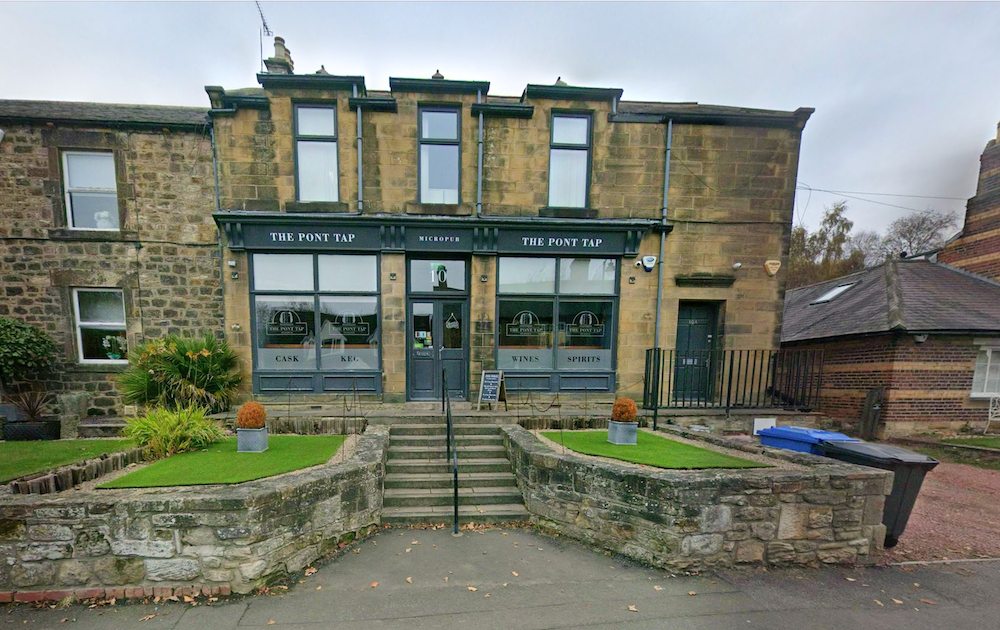 A stone building with a shopfront and bay windows, now a bar with signage reading The Pont Tap, steps up to the entrance