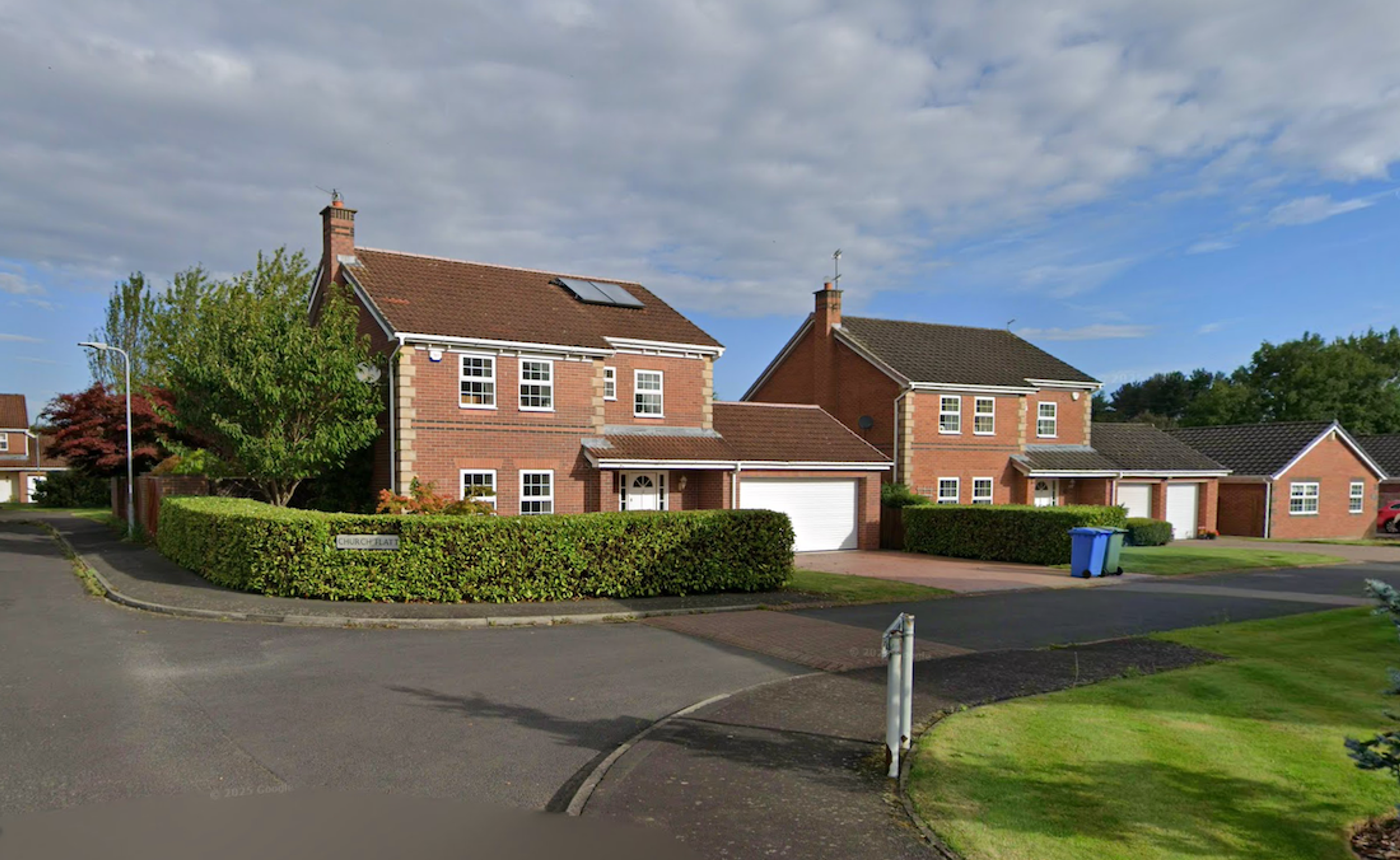Modern detached brick houses with garages and clipped hedges on a 1980s estate cul-de-sac
