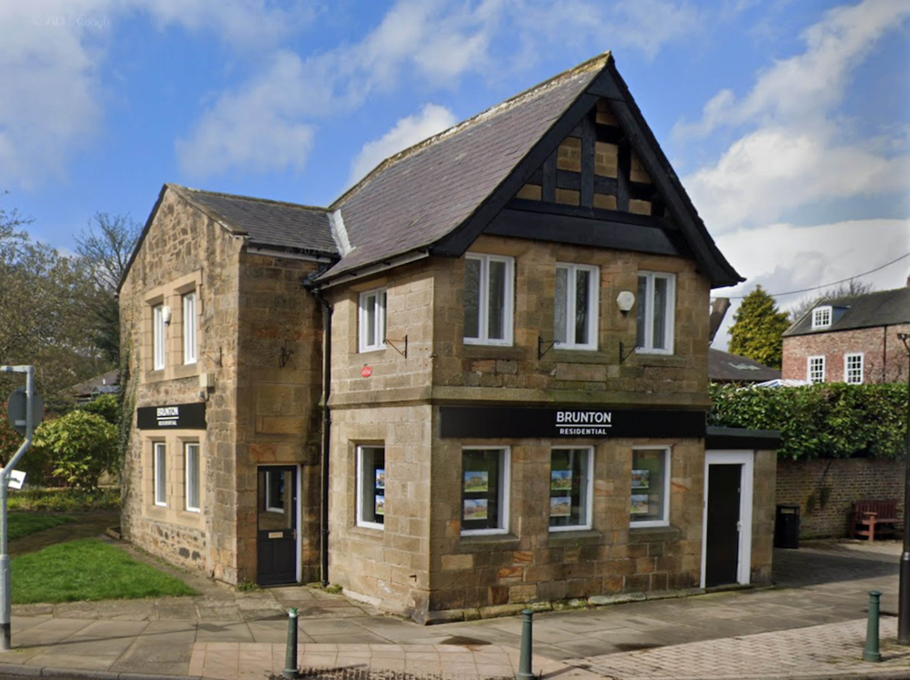 A stone building with a half-timbered gable end and slate roof on a street corner, now in use as an estate agent's office