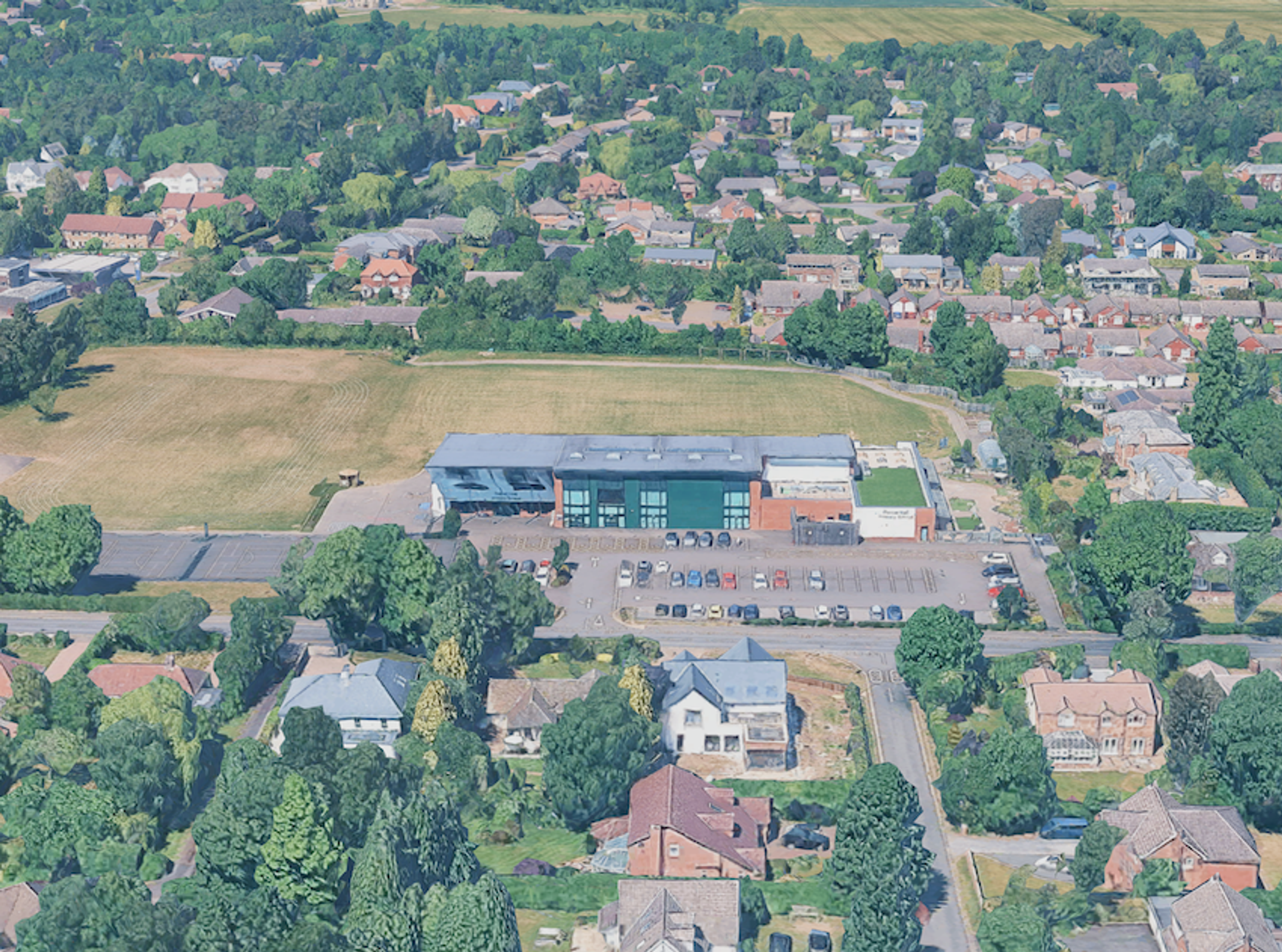 Aerial view of a modern school with a flat roof and playing field, surrounded by tree-lined suburban housing