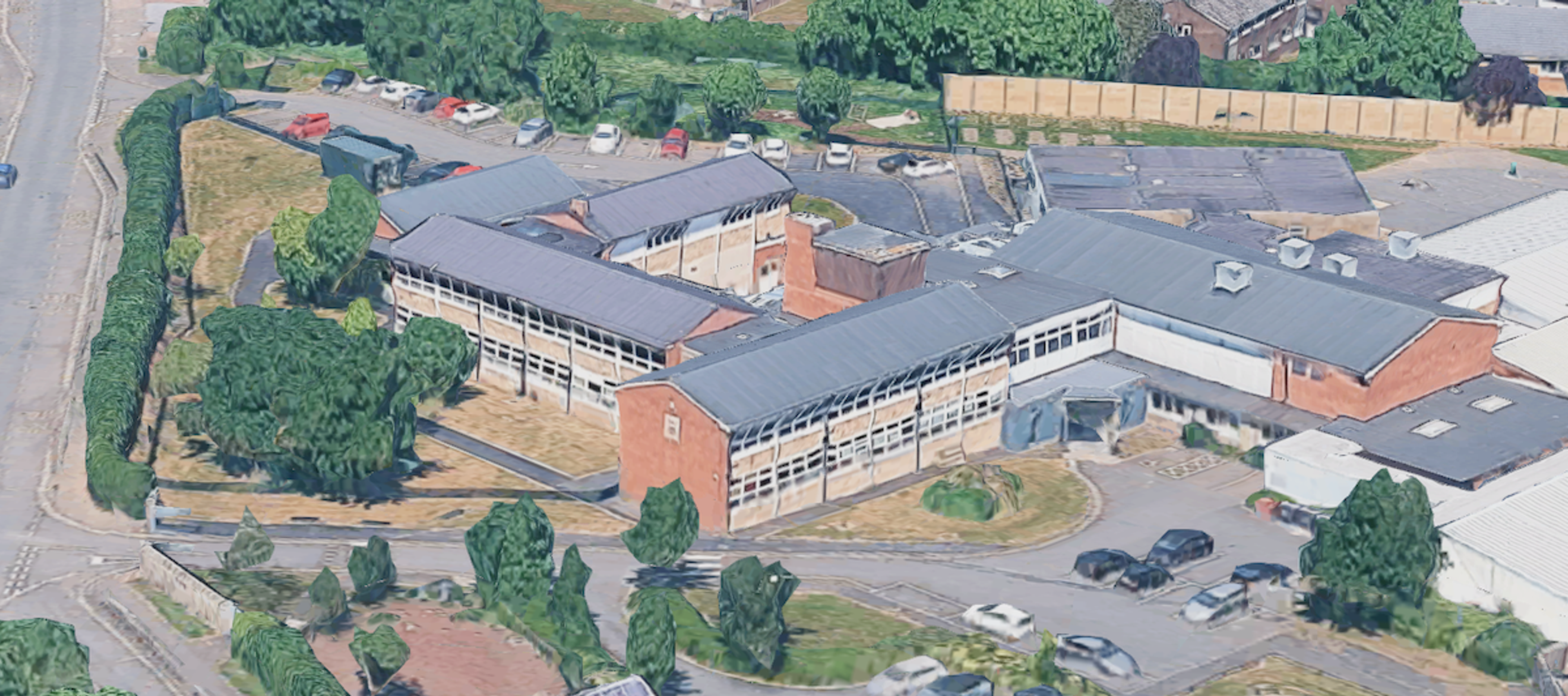 Aerial view of a flat-roofed two-storey school with long window bands, car parks and playing areas around it