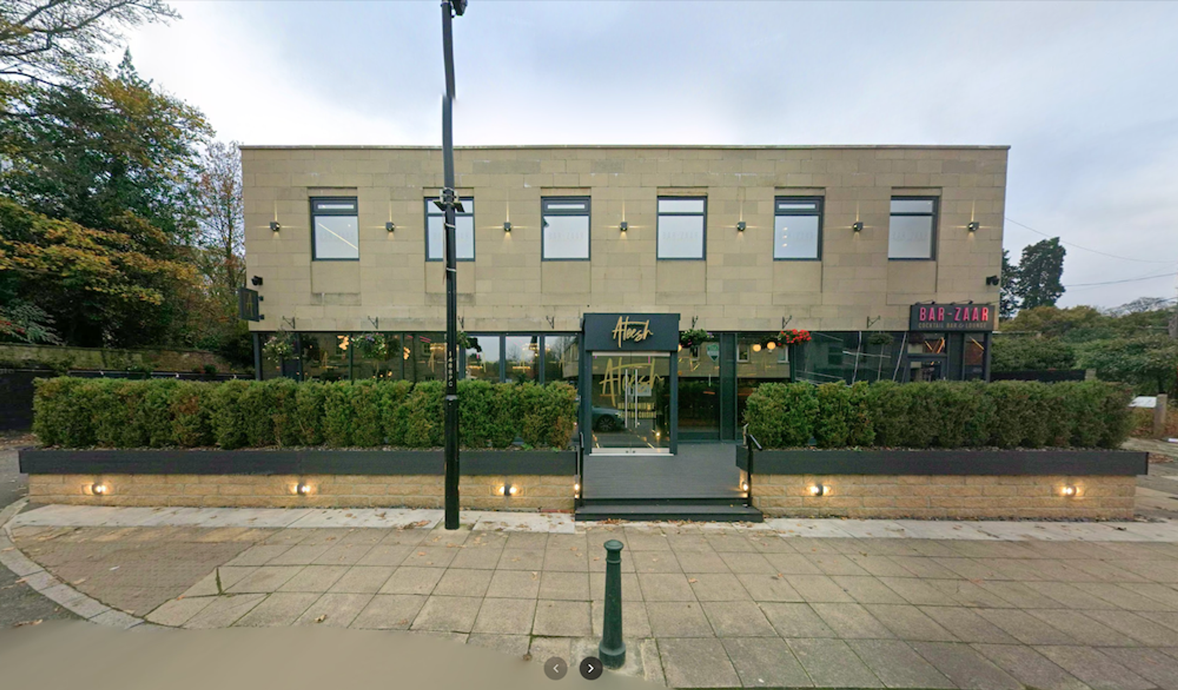 A modern two-storey stone-clad restaurant with a canopied entrance and clipped hedges along the frontage