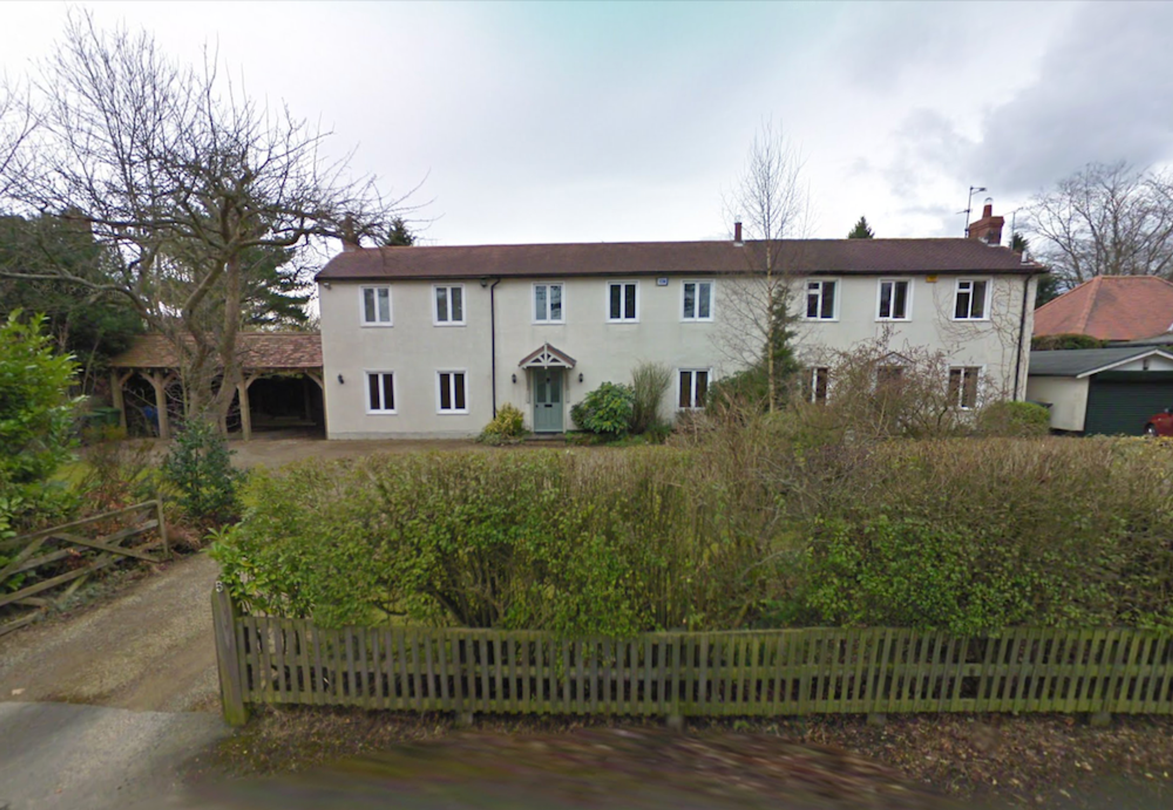 A pair of white rendered semi-detached houses with a hedge and picket fence along the roadside