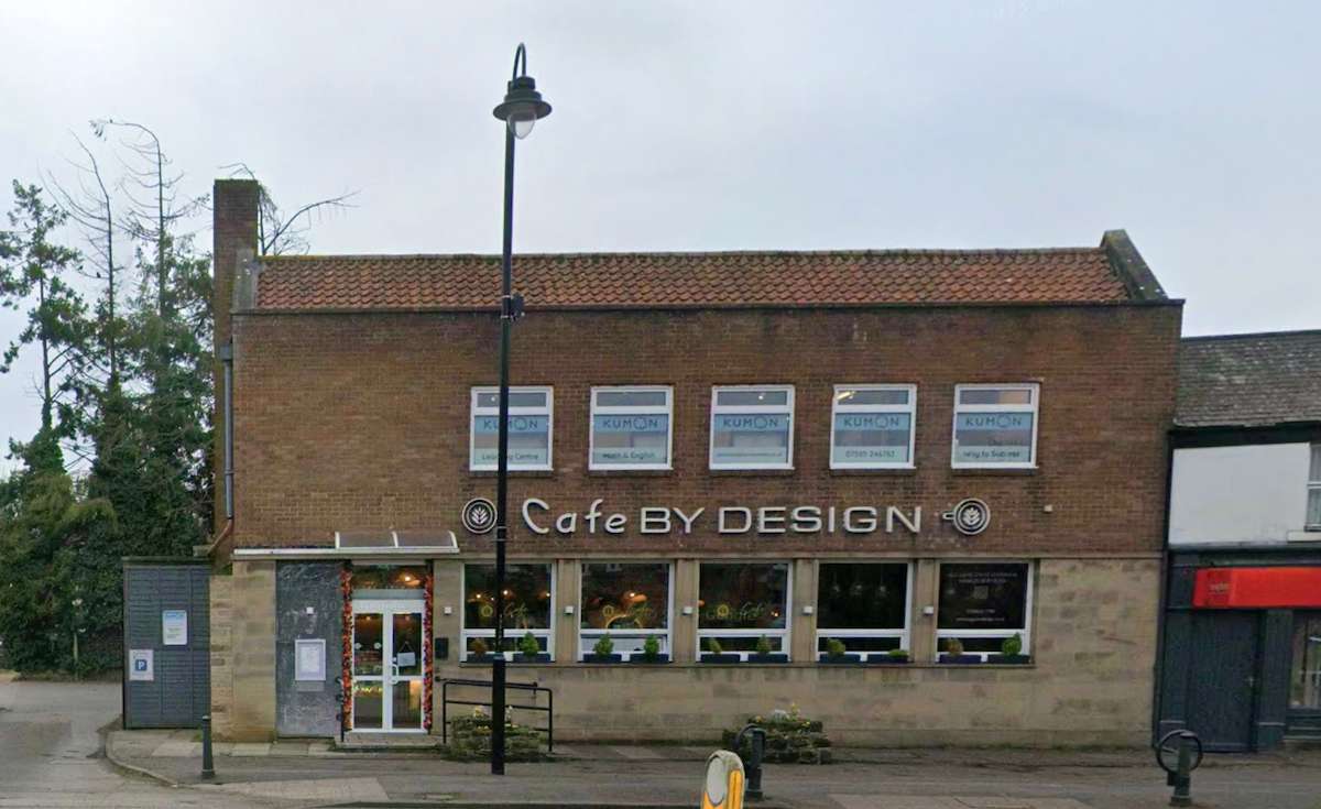 A brick building with a pantiled roof and a shopfront signed Cafe by Design, a street lamp in front