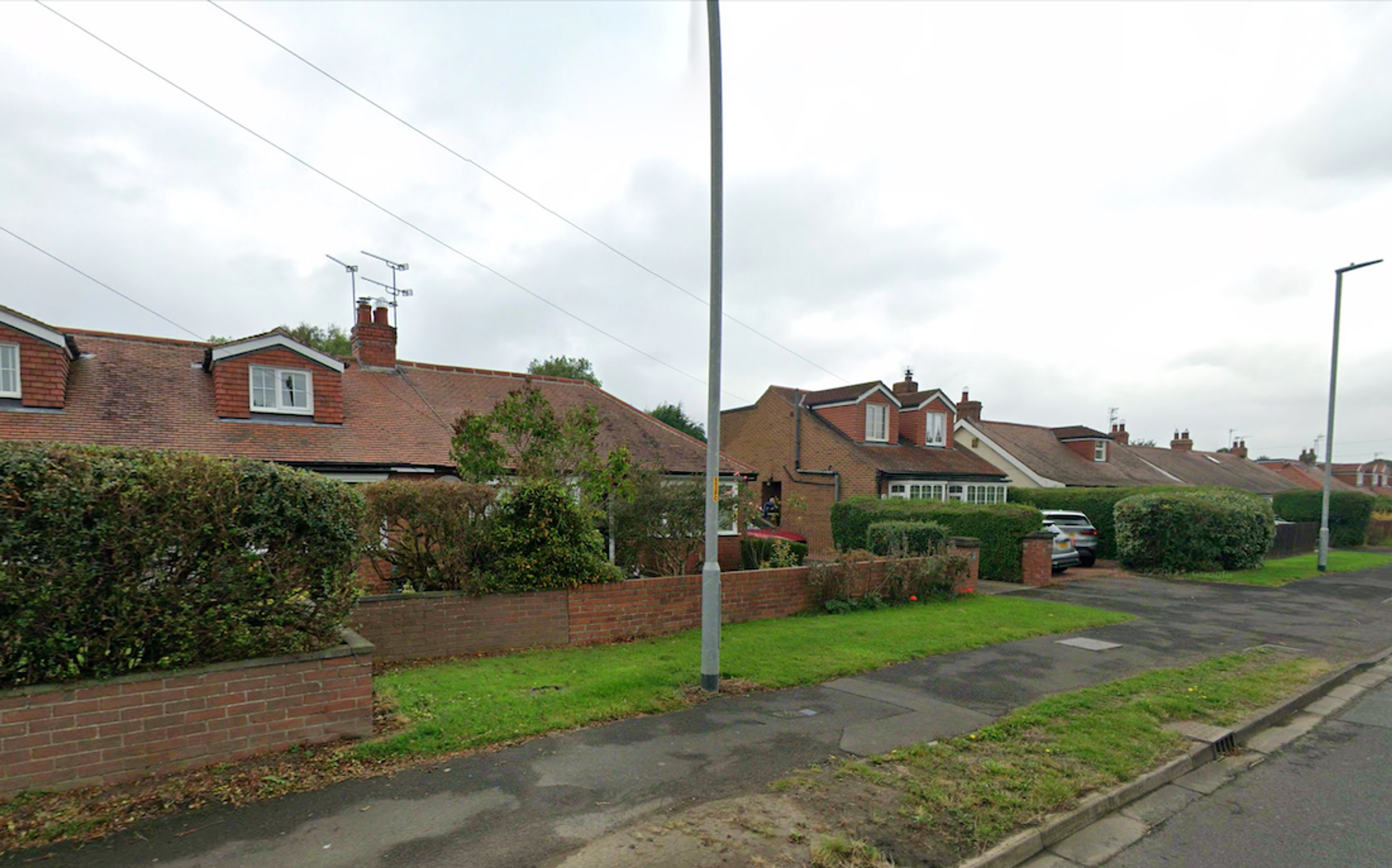 A row of brick bungalows with dormer windows and hedged front gardens along a residential street