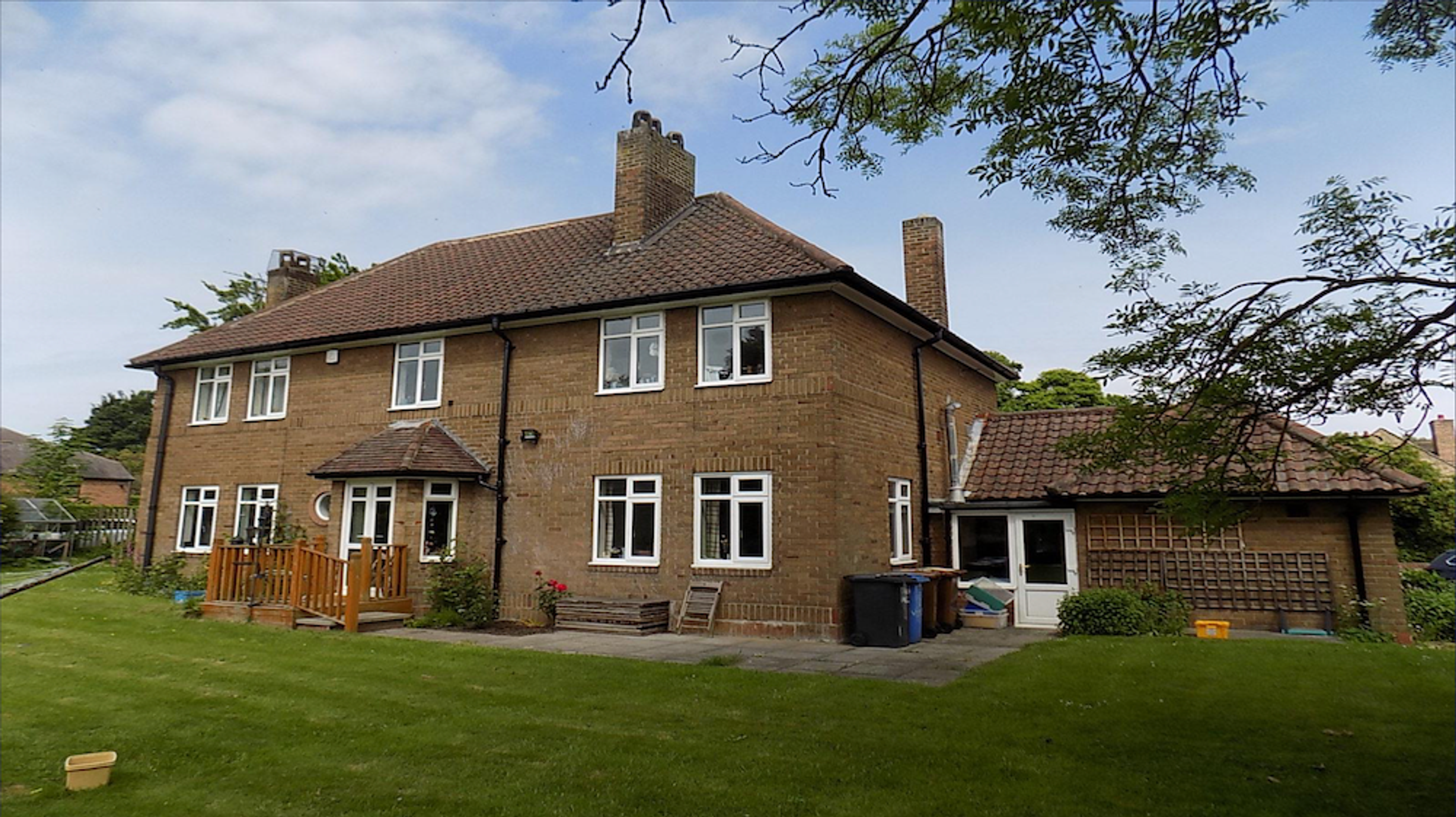 A 1950s brick house with white casement windows and tall chimneys, seen across the back lawn