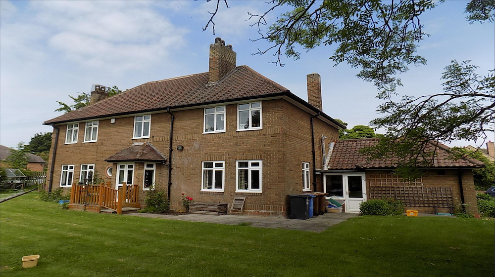 A 1950s brick house with white casement windows and tall chimneys, seen across the back lawn