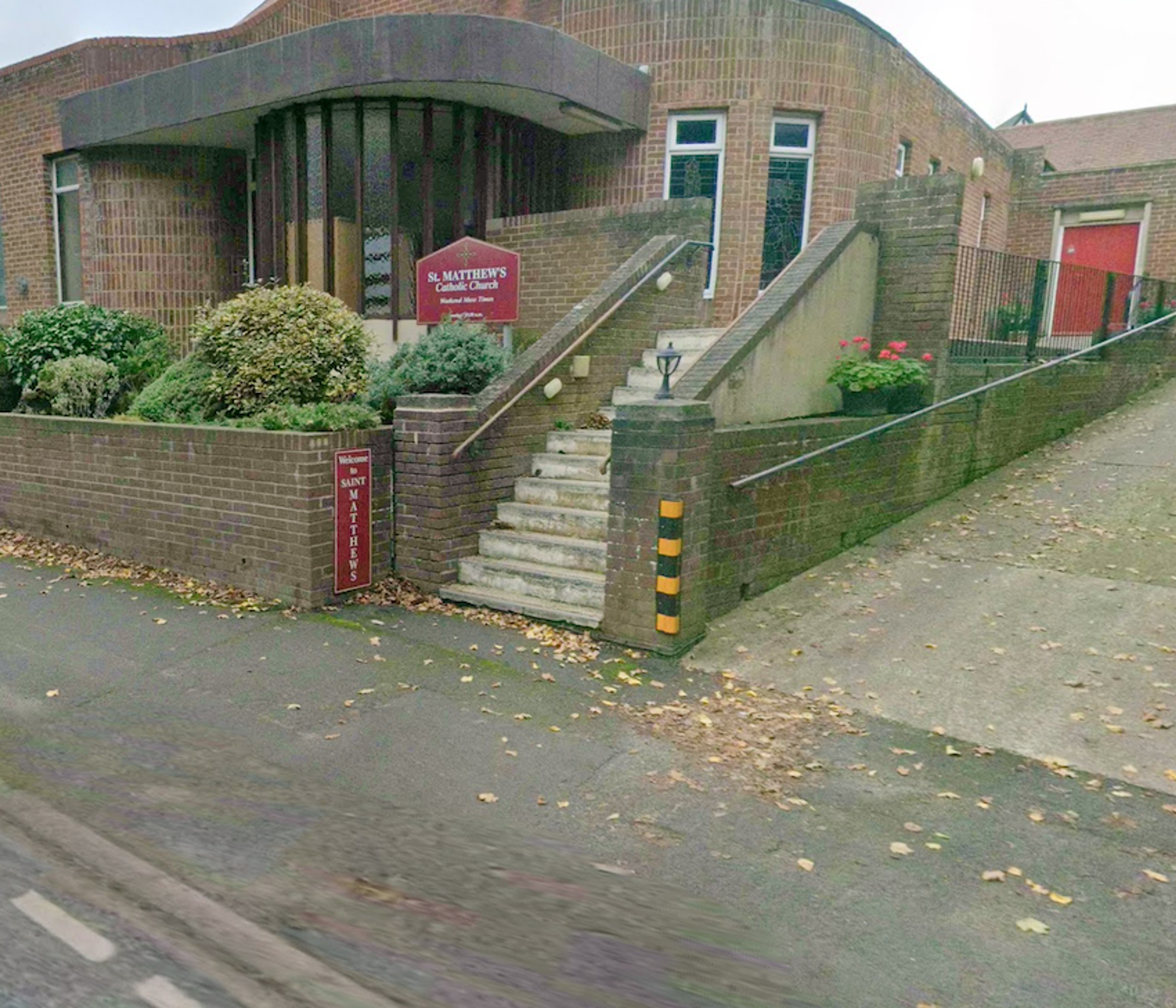 Steps and a ramp leading up from the pavement to a modern brick church with a noticeboard for St Matthew's
