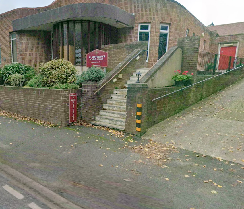 Steps and a ramp leading up from the pavement to a modern brick church with a noticeboard for St Matthew's