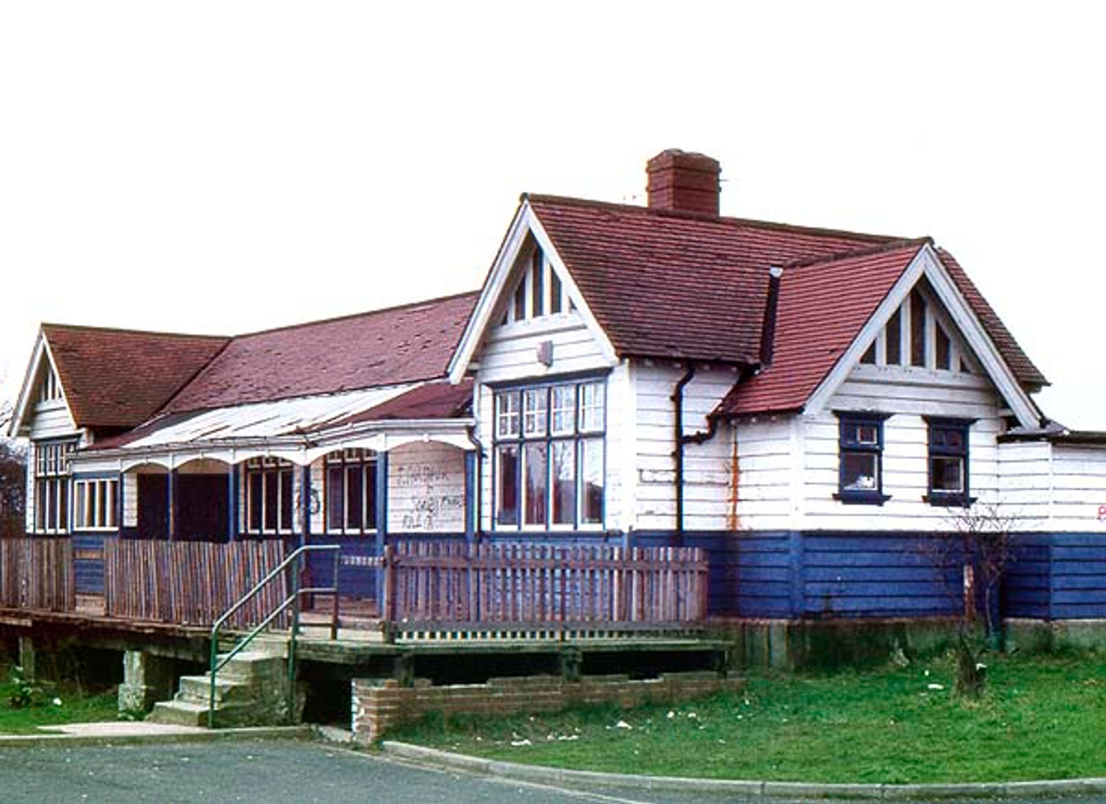 A white weatherboarded building with gabled dormers and a verandah, formerly a railway station, raised above the roadside