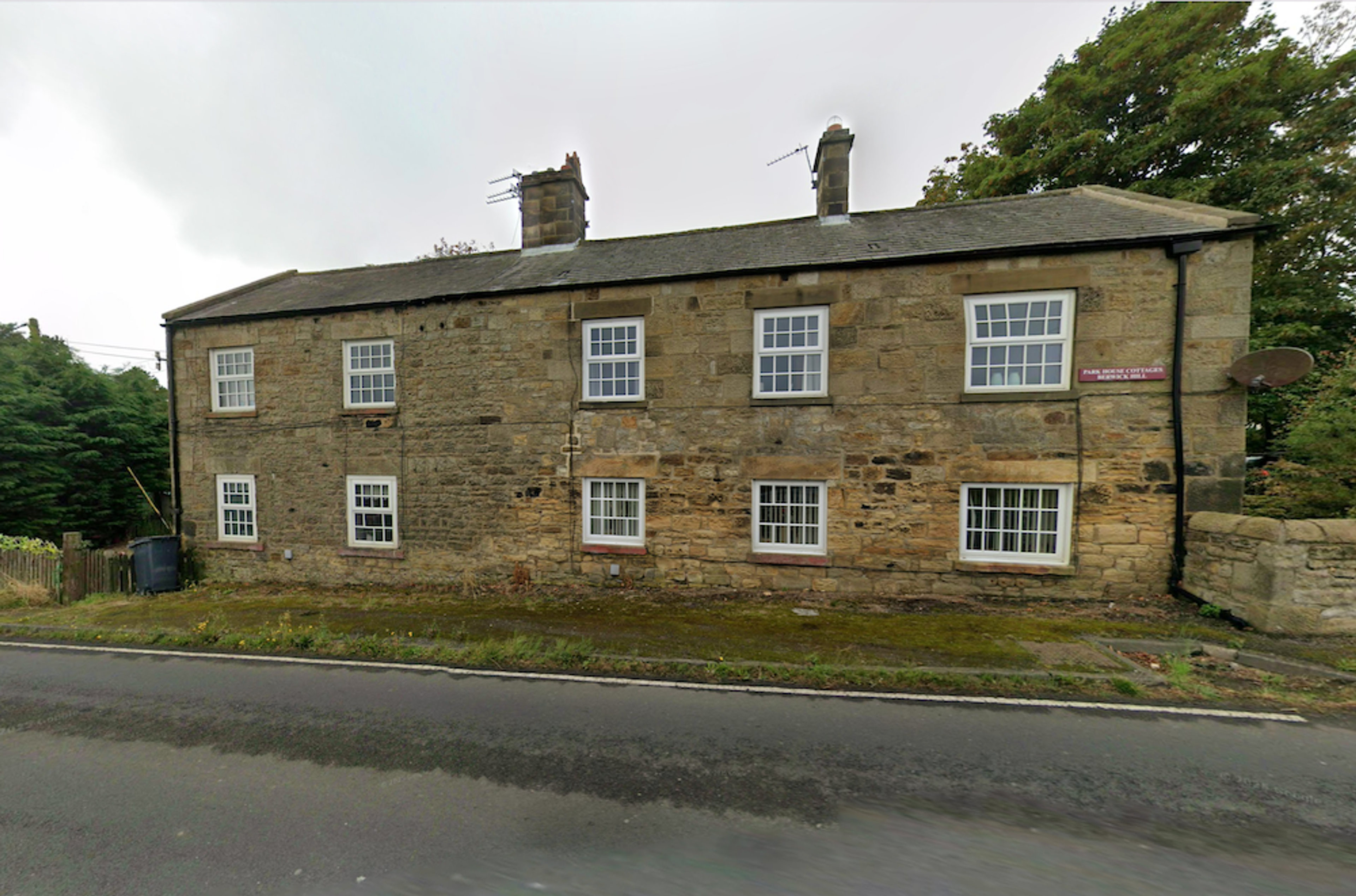 A two-storey stone cottage terrace with white sash windows, standing directly on the roadside