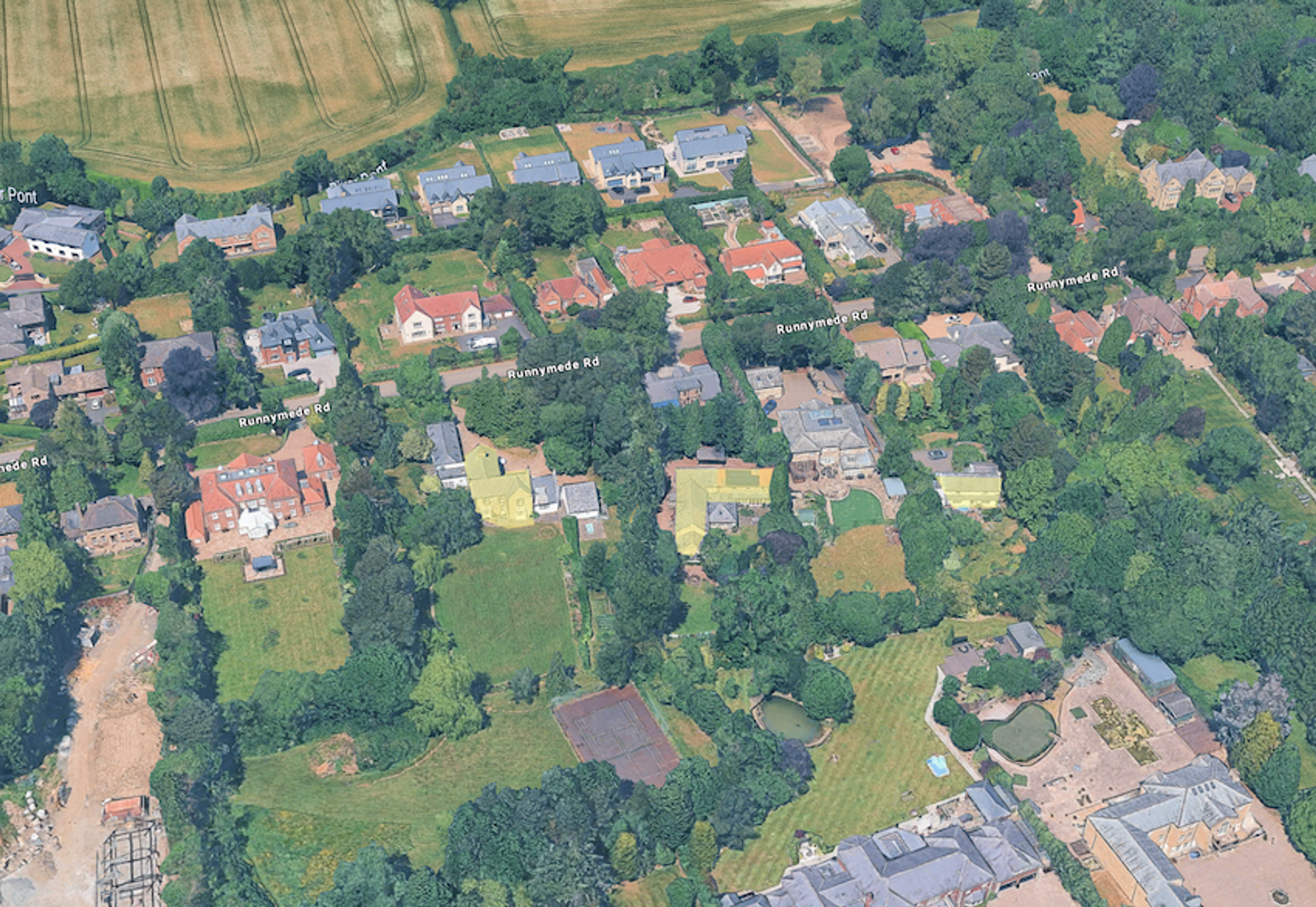 Aerial view of large detached houses in wooded gardens, with open farmland beyond