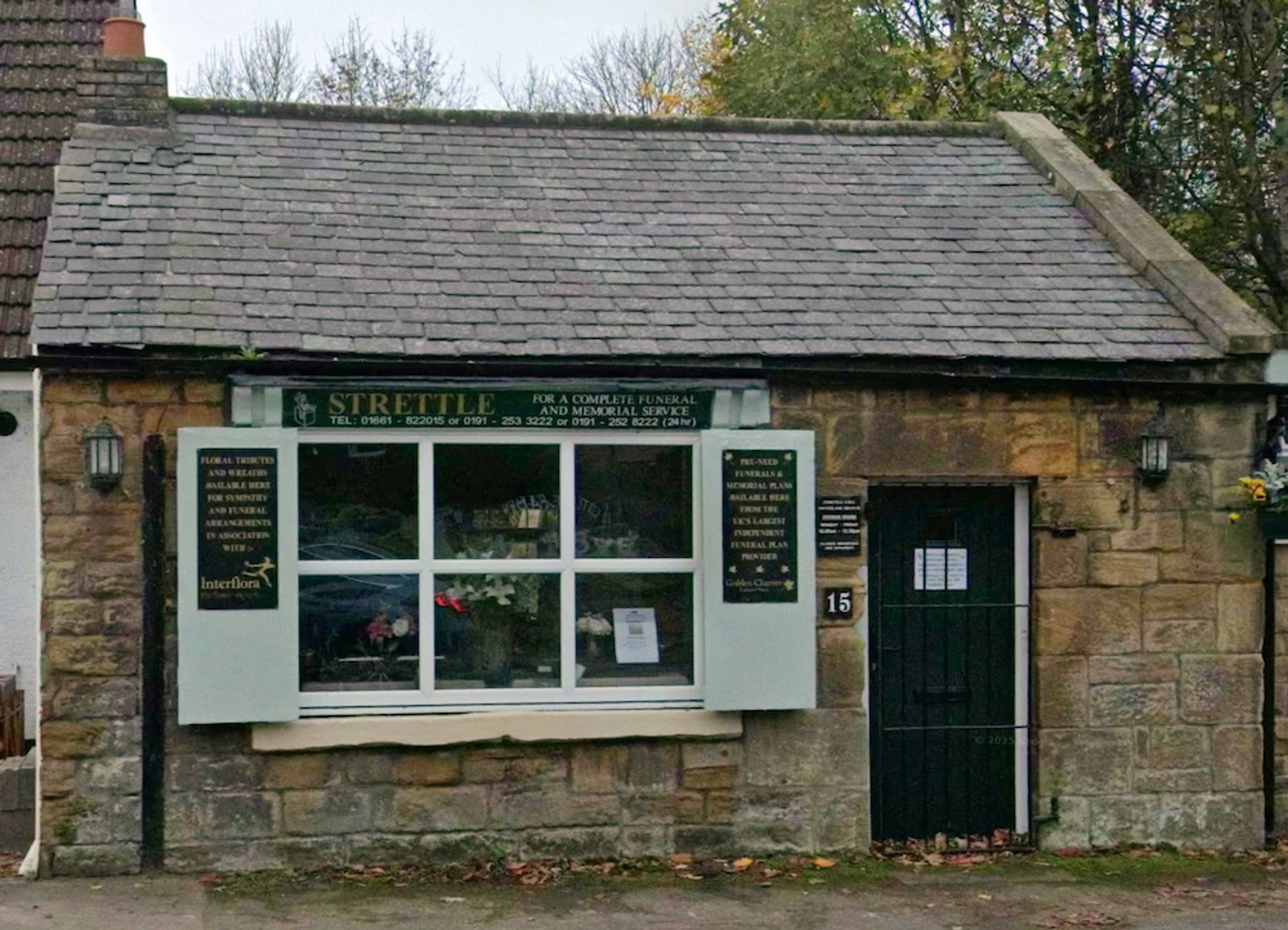 A small single-storey stone building with a slate roof, its shopfront window carrying a florist's and funeral director's sign