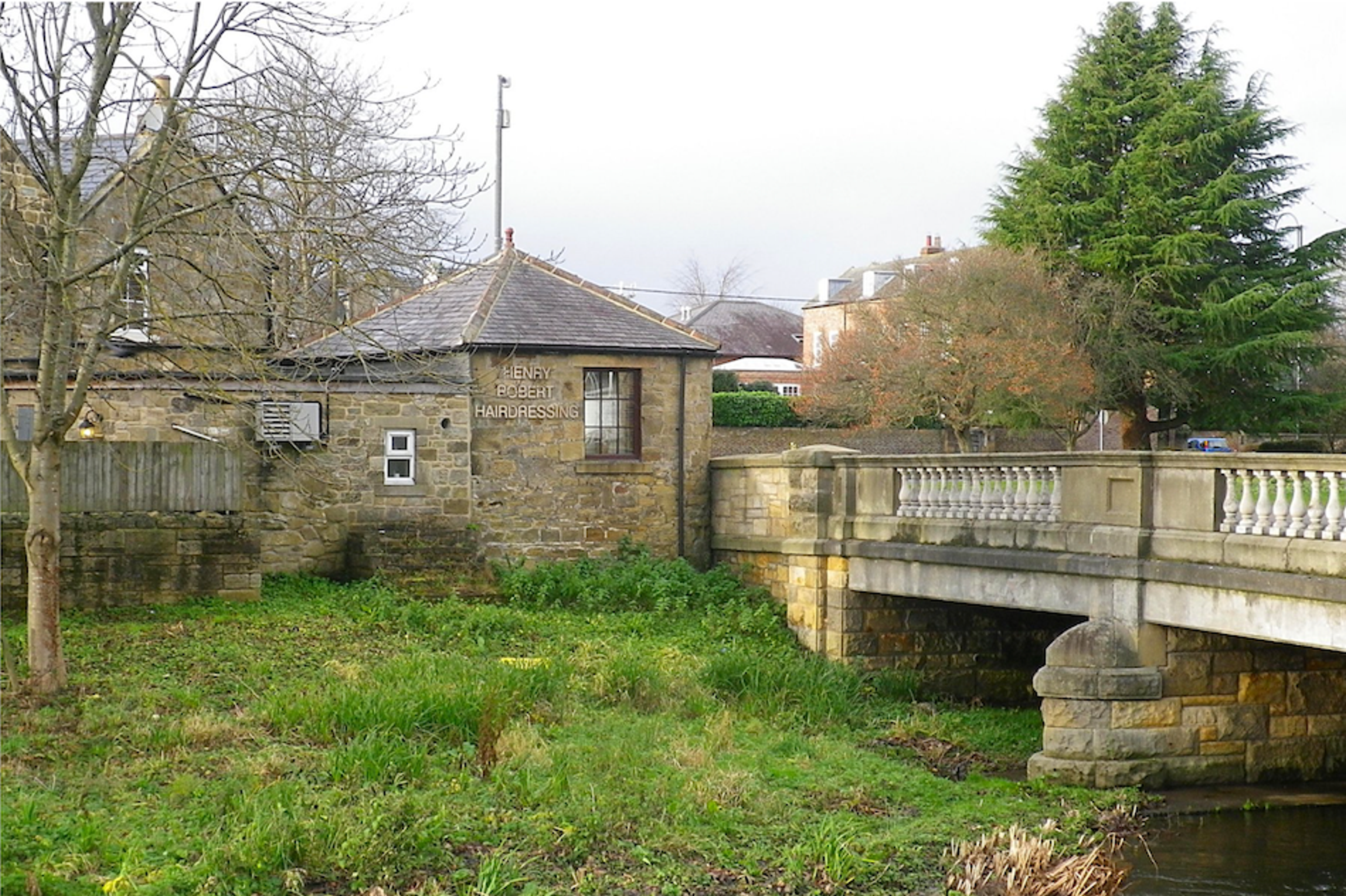 A small square stone building with a pyramidal roof standing at the end of a balustraded road bridge over a river