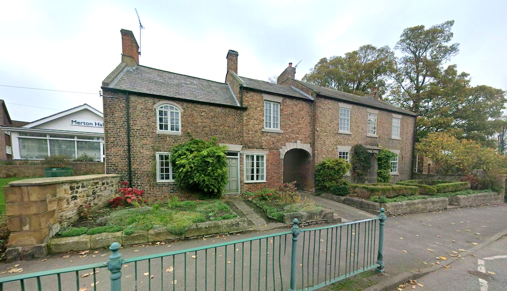 A brick and stone house with an arched carriage entrance and terraced front garden, behind green iron railings